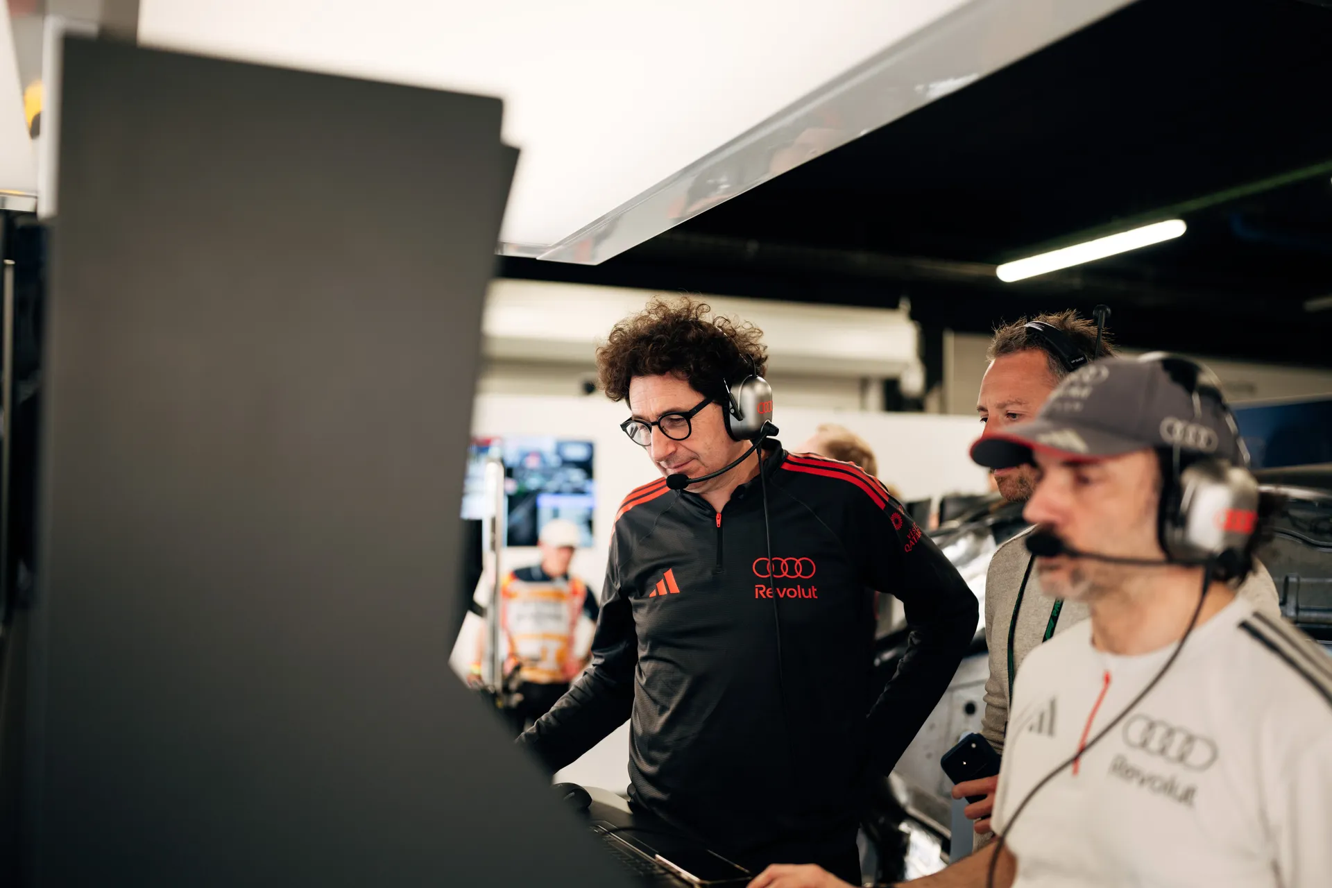 Mattia Binotto monitoring data on a screen with Audi Revolut F1® Team engineers wearing headsets inside the Barcelona garage