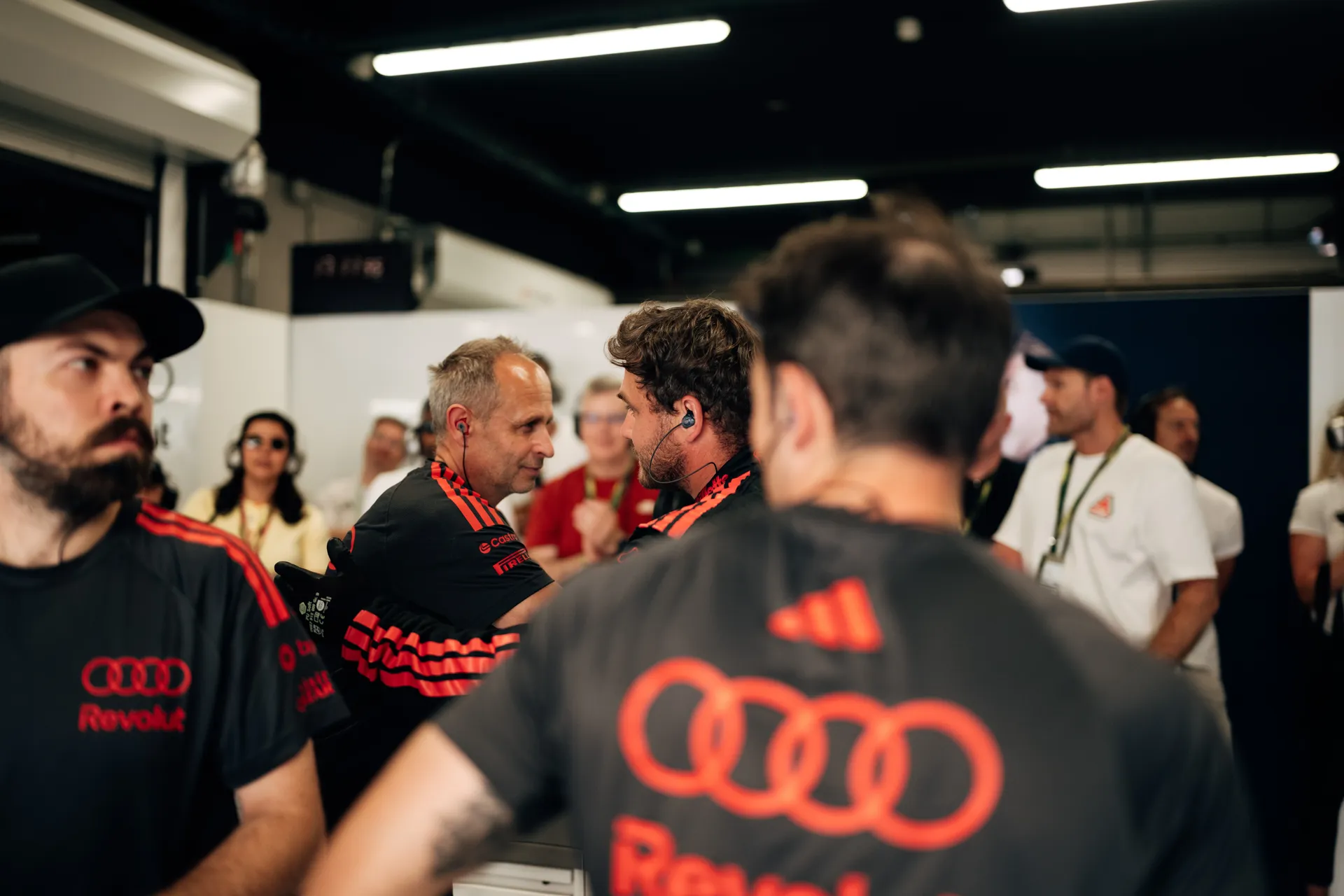 Audi Revolut F1® Team crew members in discussion inside the garage during qualifying, surrounded by engineers and team staff in the background