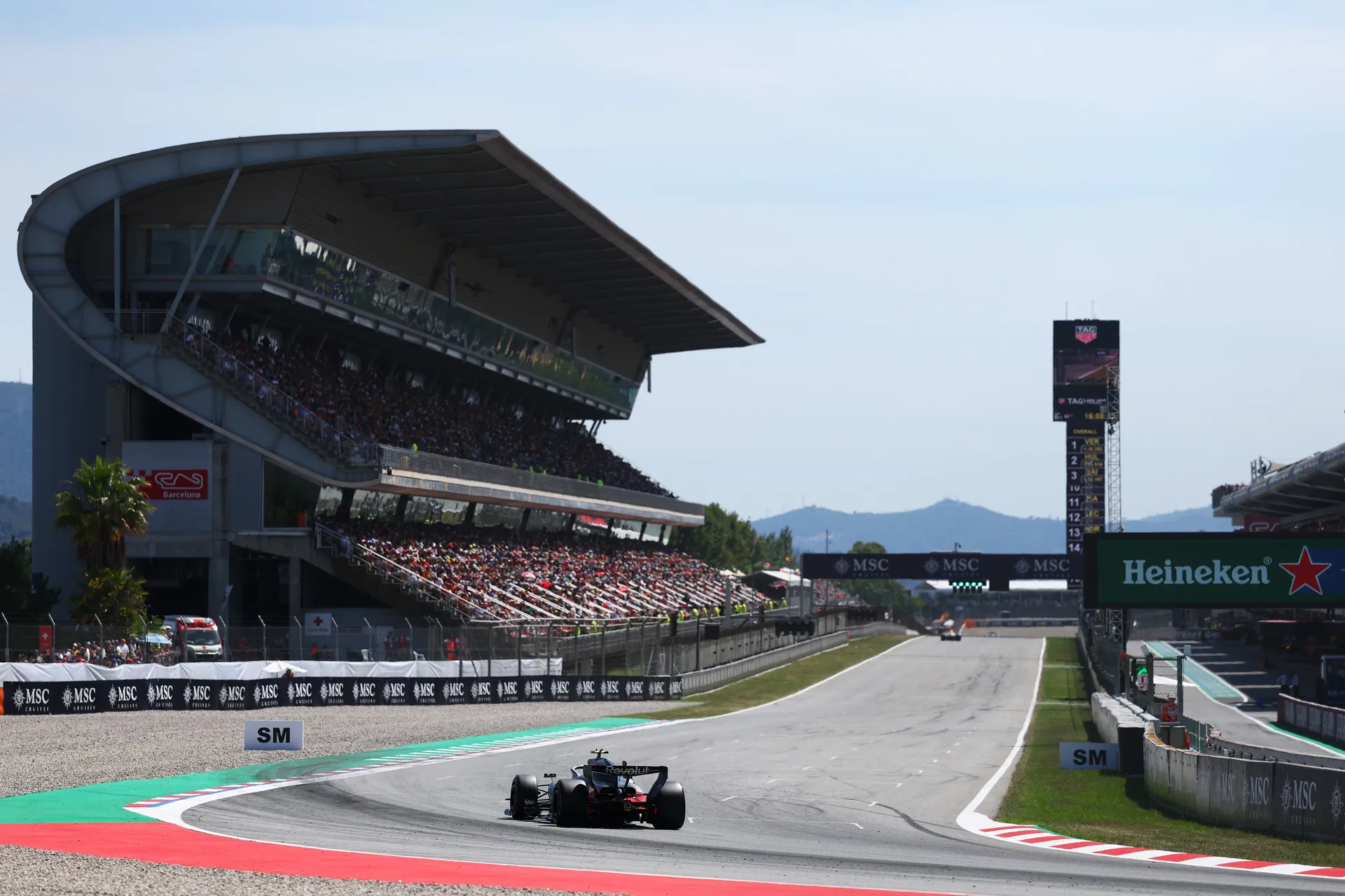 Audi Revolut F1® Team car exiting the final corner onto the main straight in Barcelona, with full grandstands and the pit complex visible under clear race-day conditions.