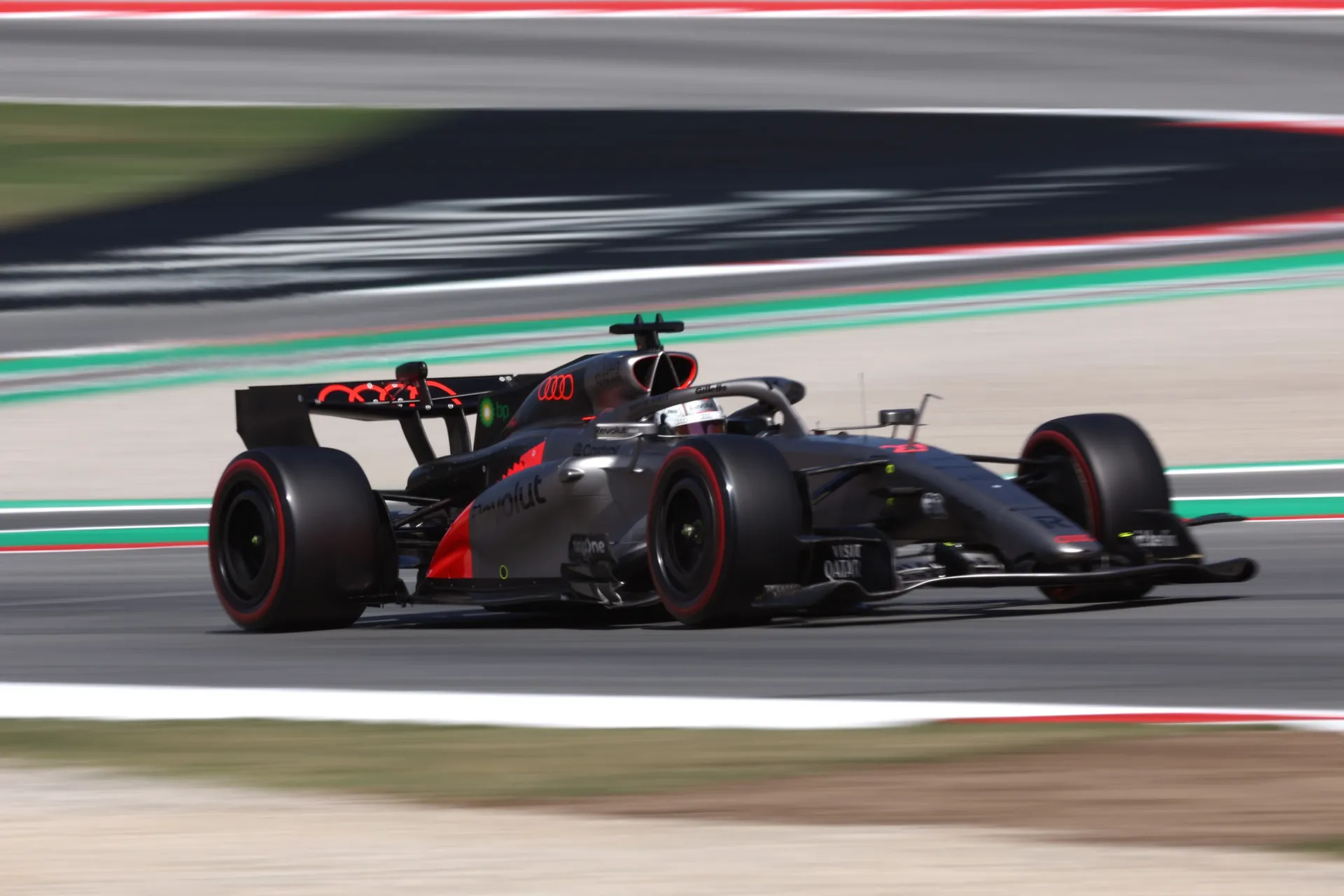 Side-on panning shot of an Audi Revolut F1® Team car navigating a fast corner, highlighting aerodynamic flow, tire deformation and on-track precision.