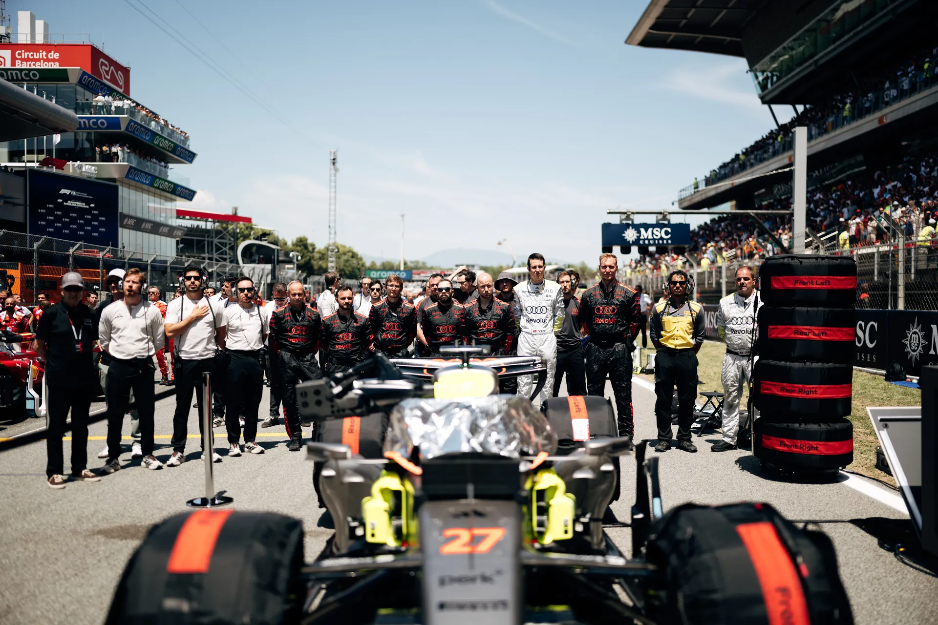 Audi R26 with car number 27 positioned on the Barcelona grid with Audi Revolut F1® Team members lined up behind.