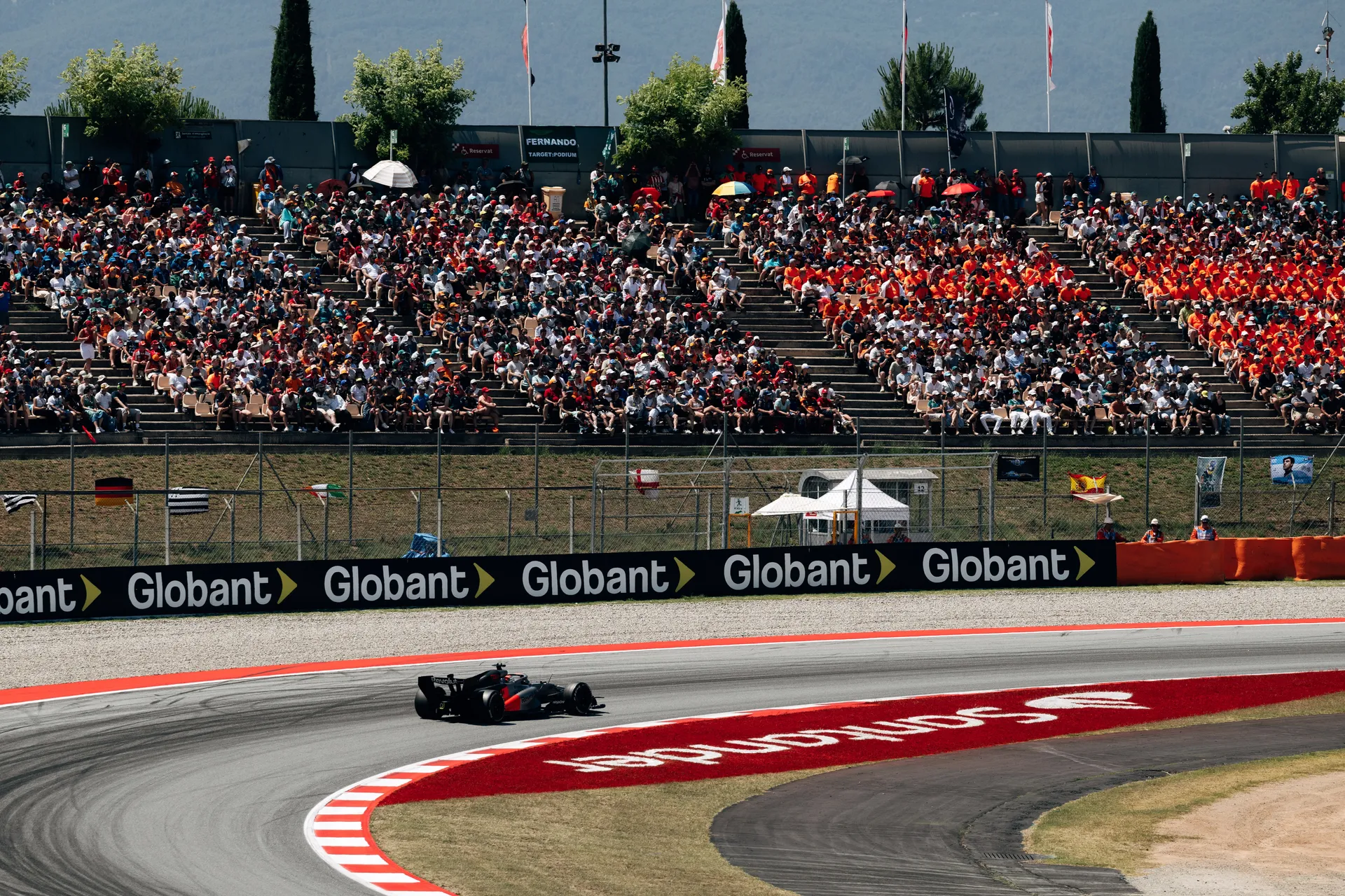 Audi R26 driving through a sweeping corner at Circuit de Barcelona-Catalunya with grandstands full of spectators in the background.