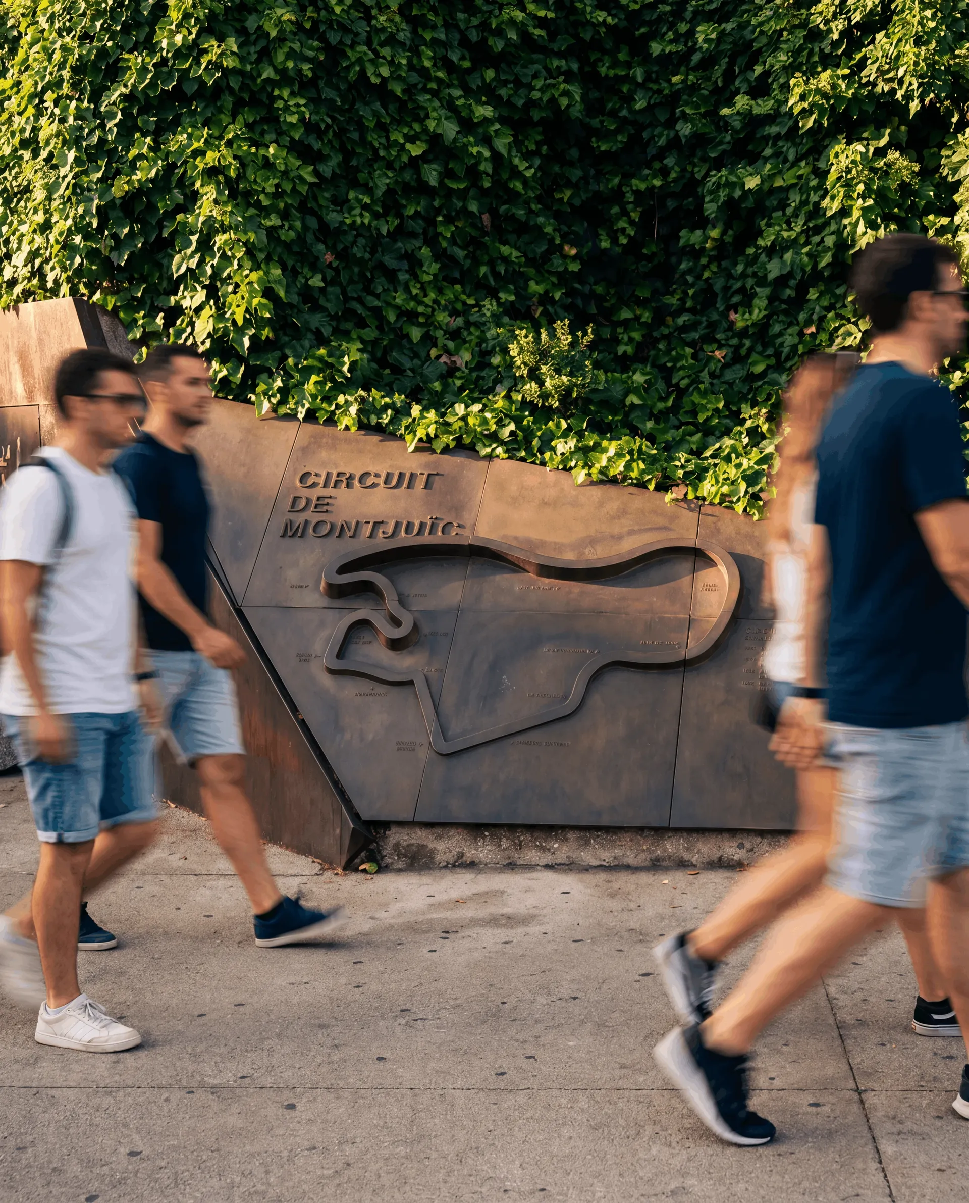 Passers-by walking past the Circuit de Montjuïc memorial with the track layout in relief