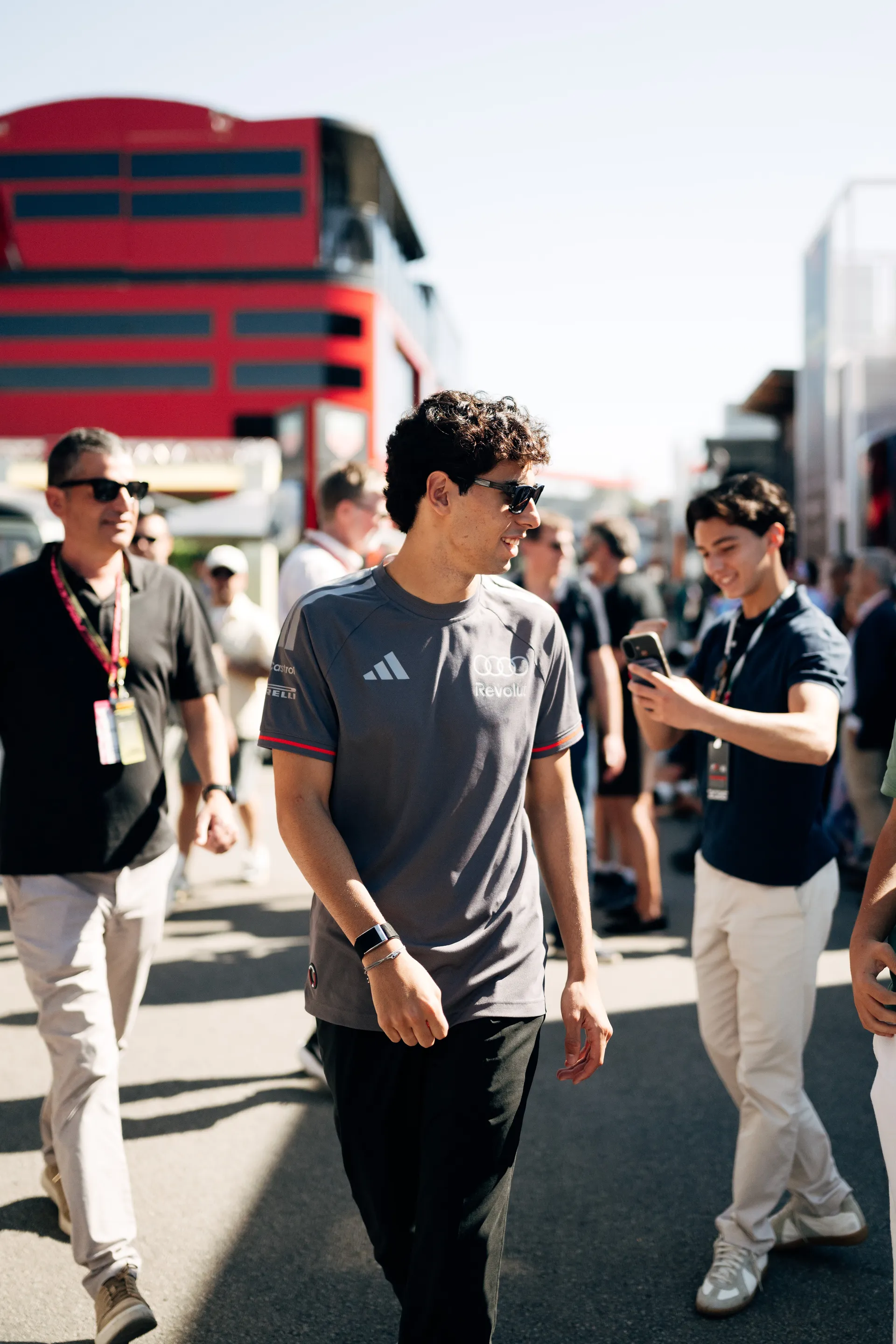 Gabriel Bortoleto walking through the paddock in Audi Revolut F1® Team apparel, looking to the side while fans and team personnel surround him.
