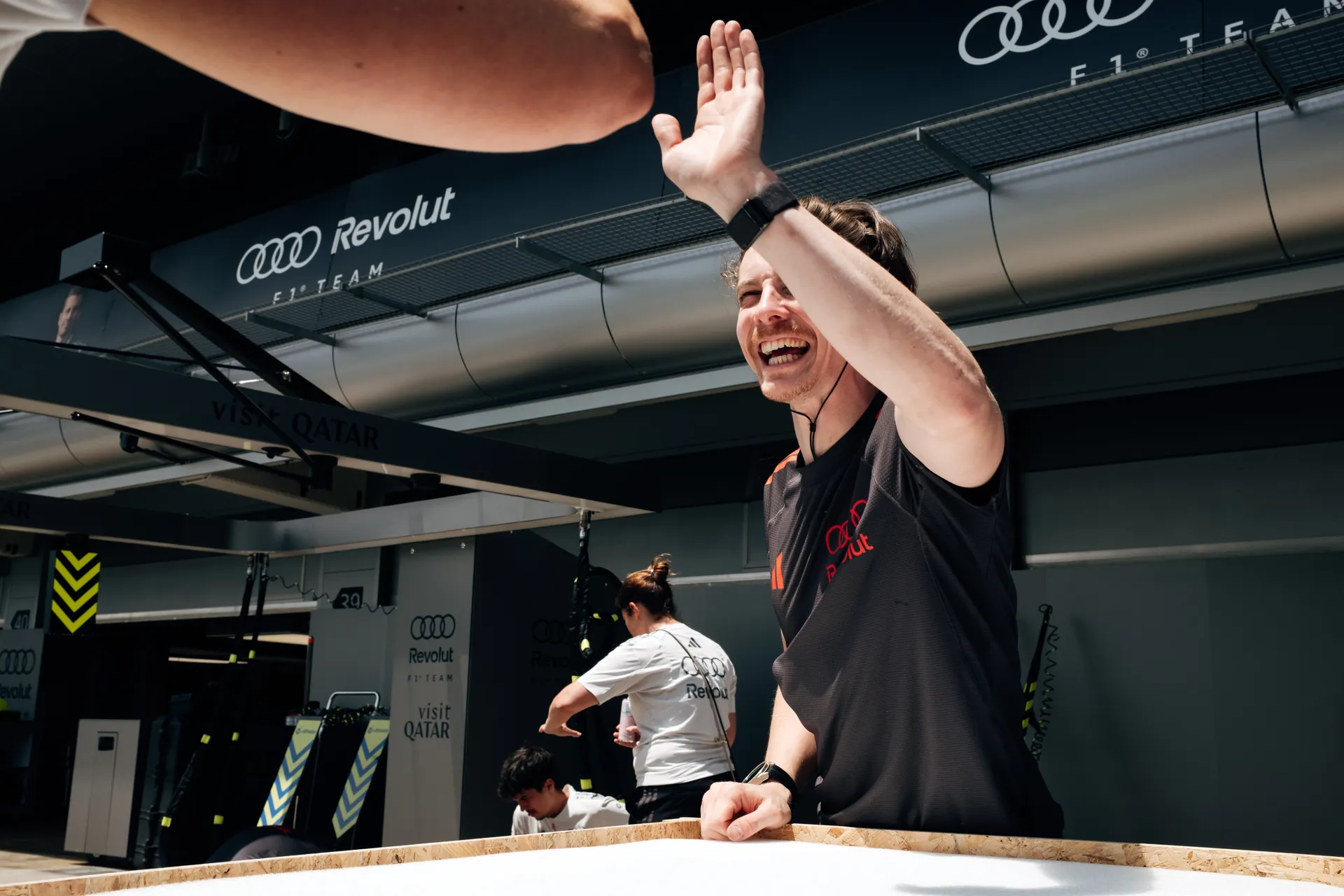 Audi Revolut F1® Team crew member celebrates with a raised hand inside the garage, reacting to a moment during setup or session.