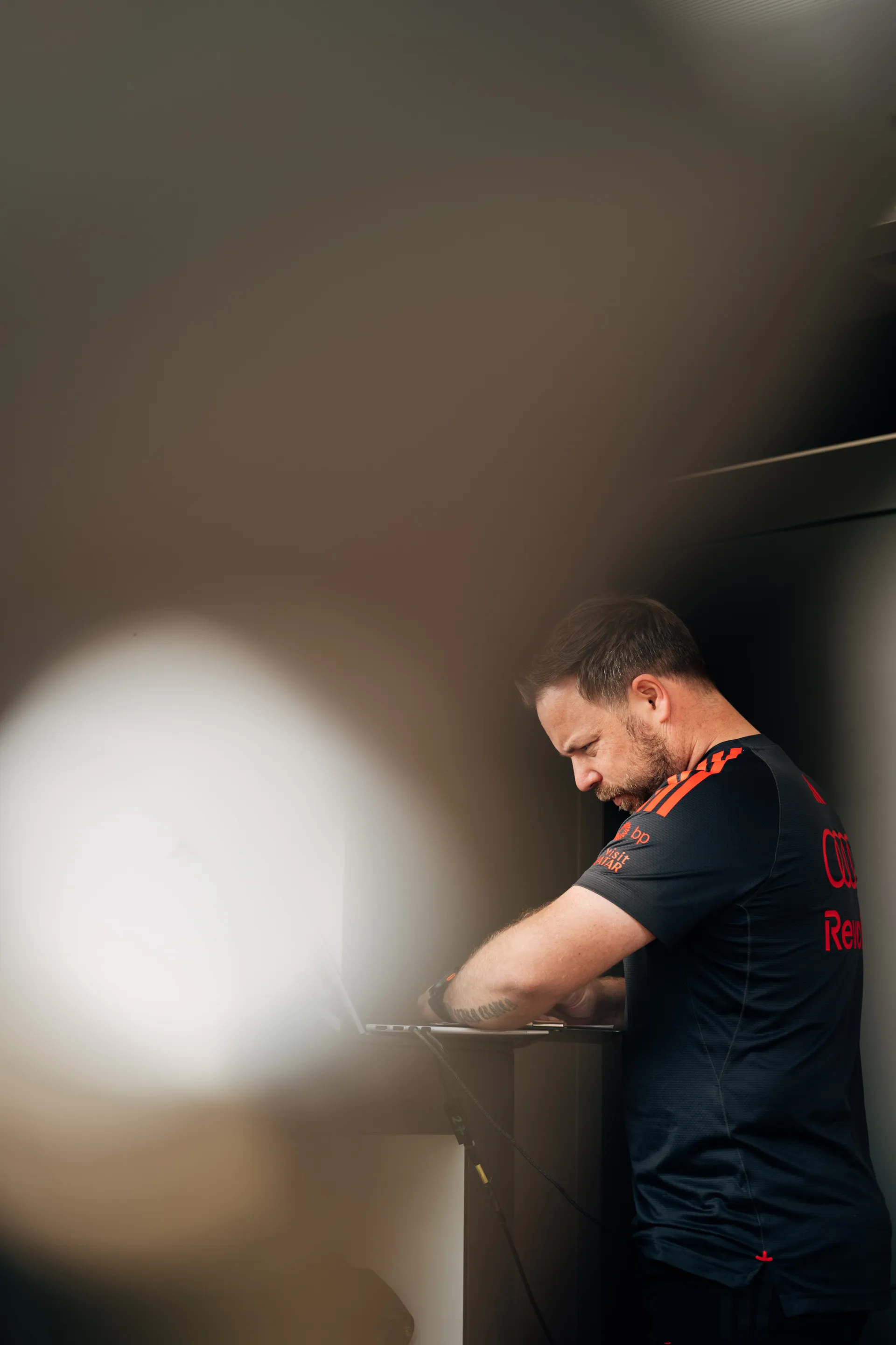 Audi Revolut F1® Team engineer works on a laptop at a standing desk, partially obscured, focused on data analysis in the garage.