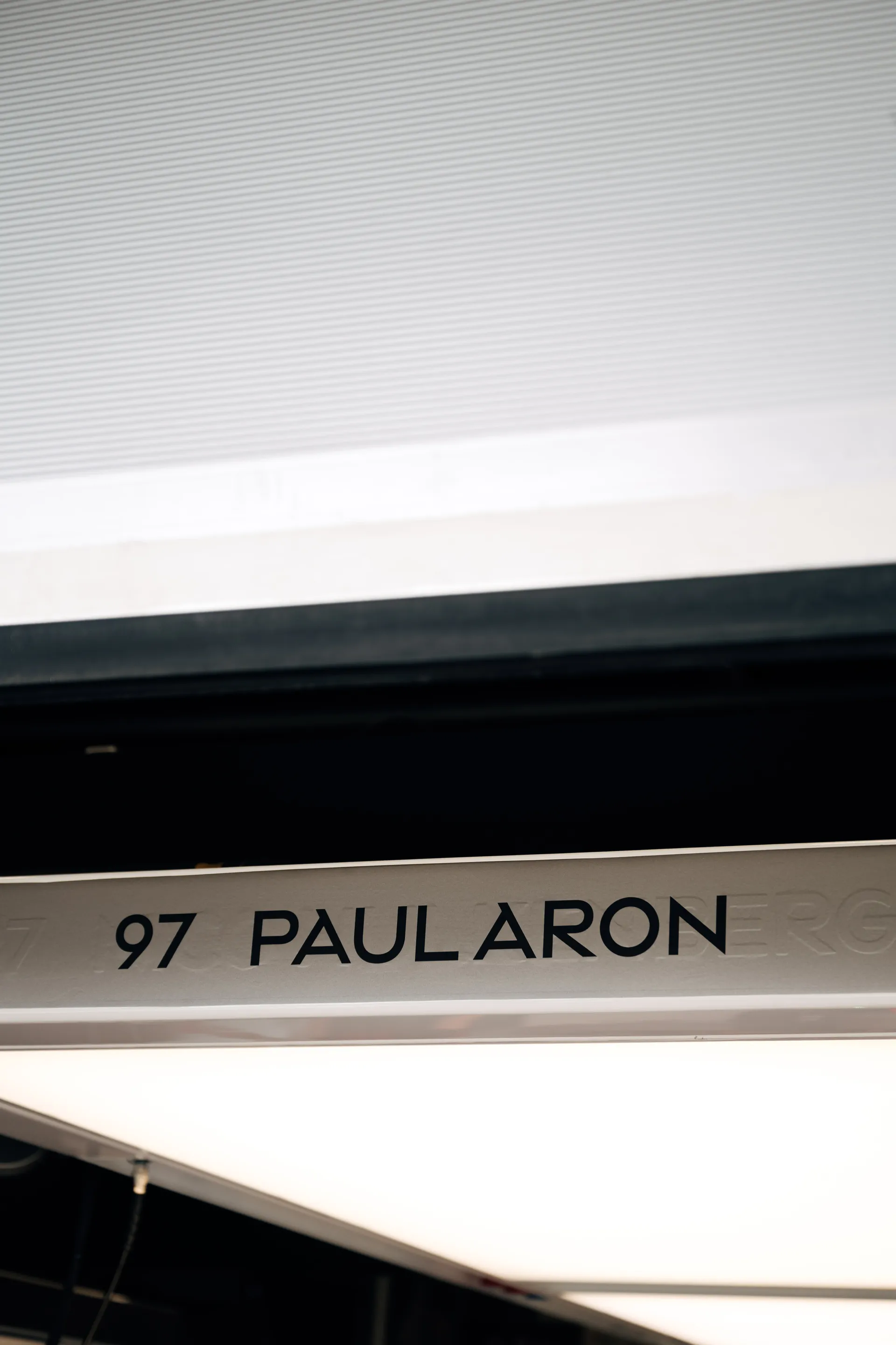 Garage signage displaying “97 Paul Aron” above a workstation, indicating the young driver’s assigned position.