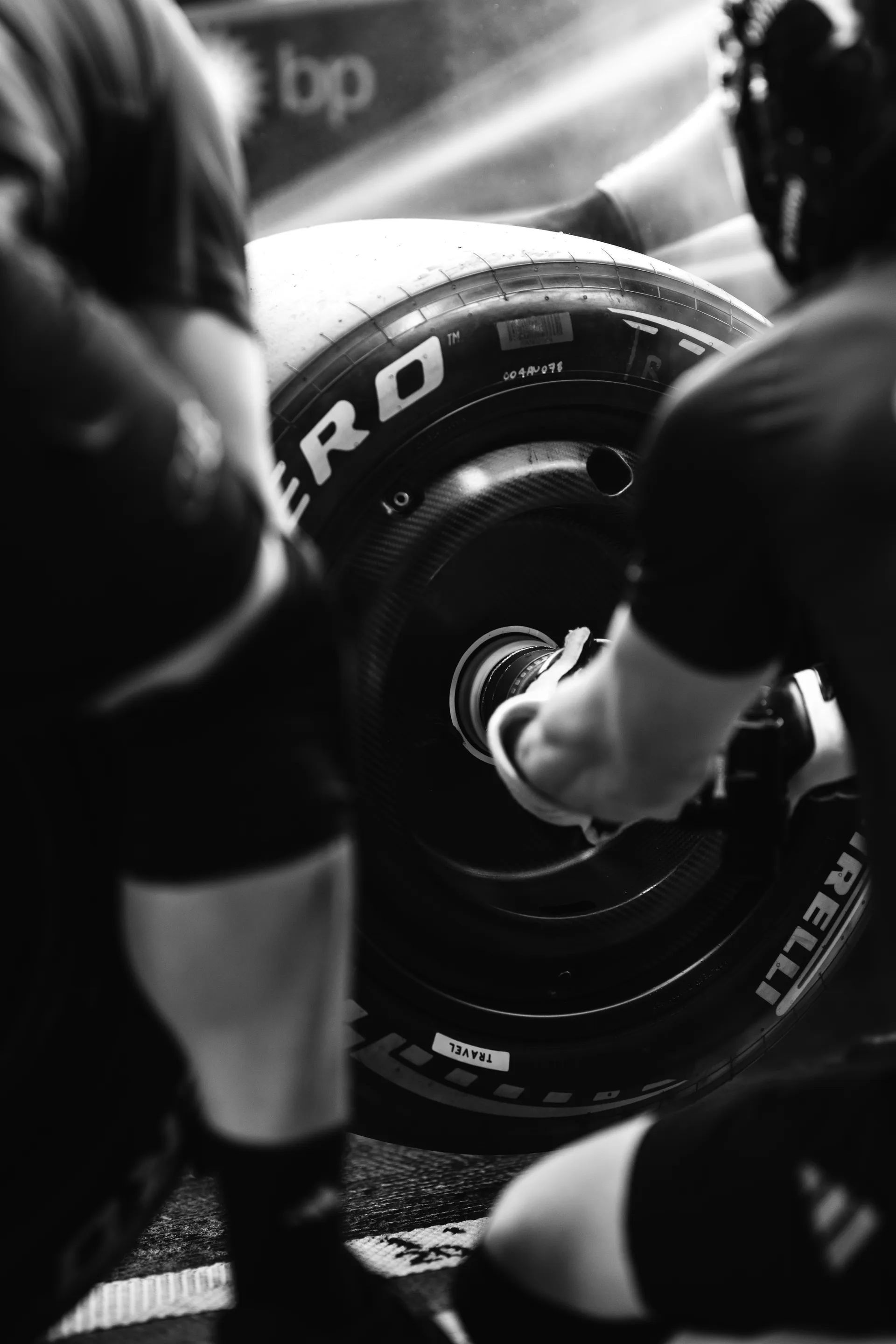 Black and white close-up of Audi Revolut F1® Team mechanics fitting a Pirelli tire onto the wheel hub during a pit stop drill.