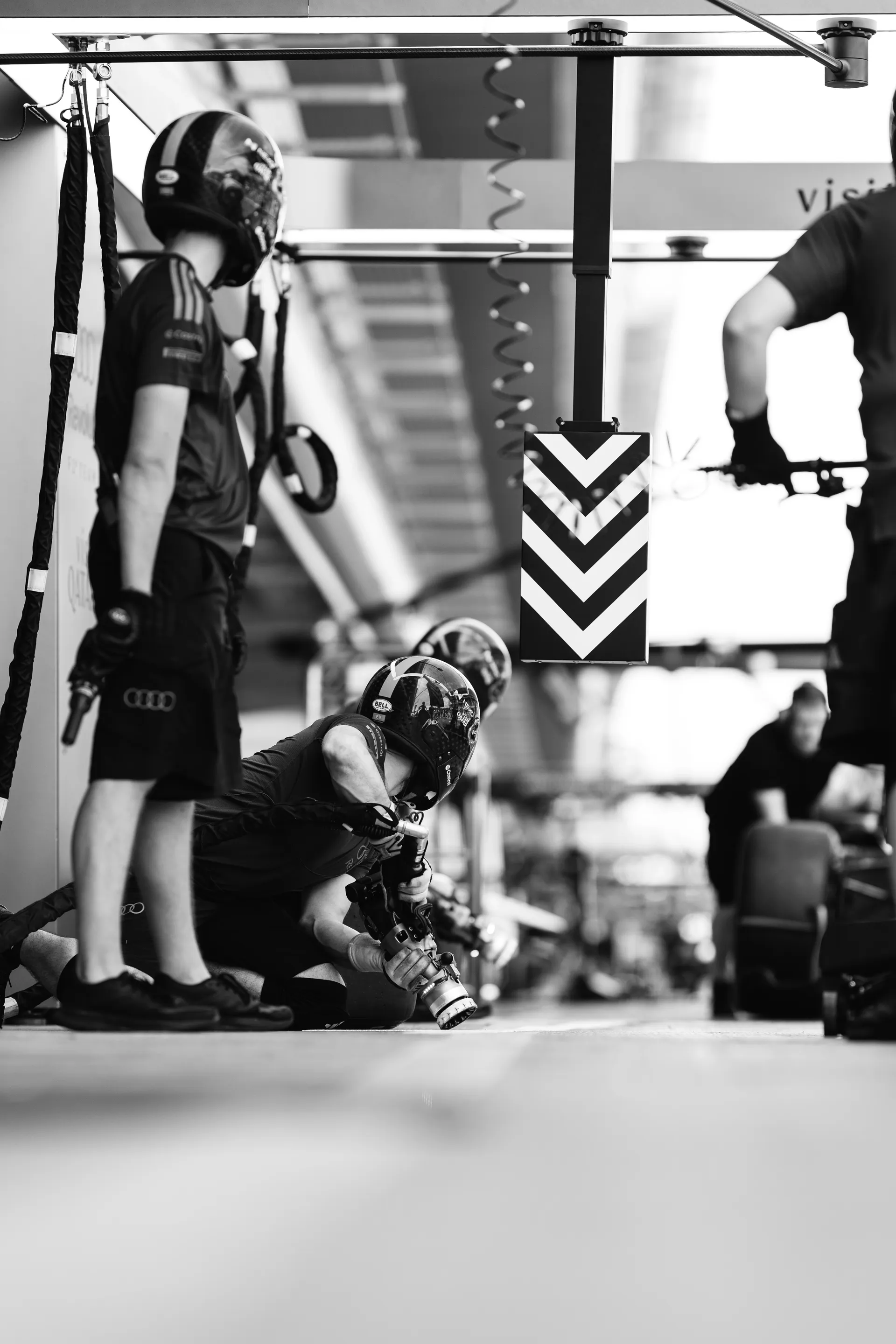 Black and white image of a pit crew member crouched with equipment, preparing for a practice pit stop.