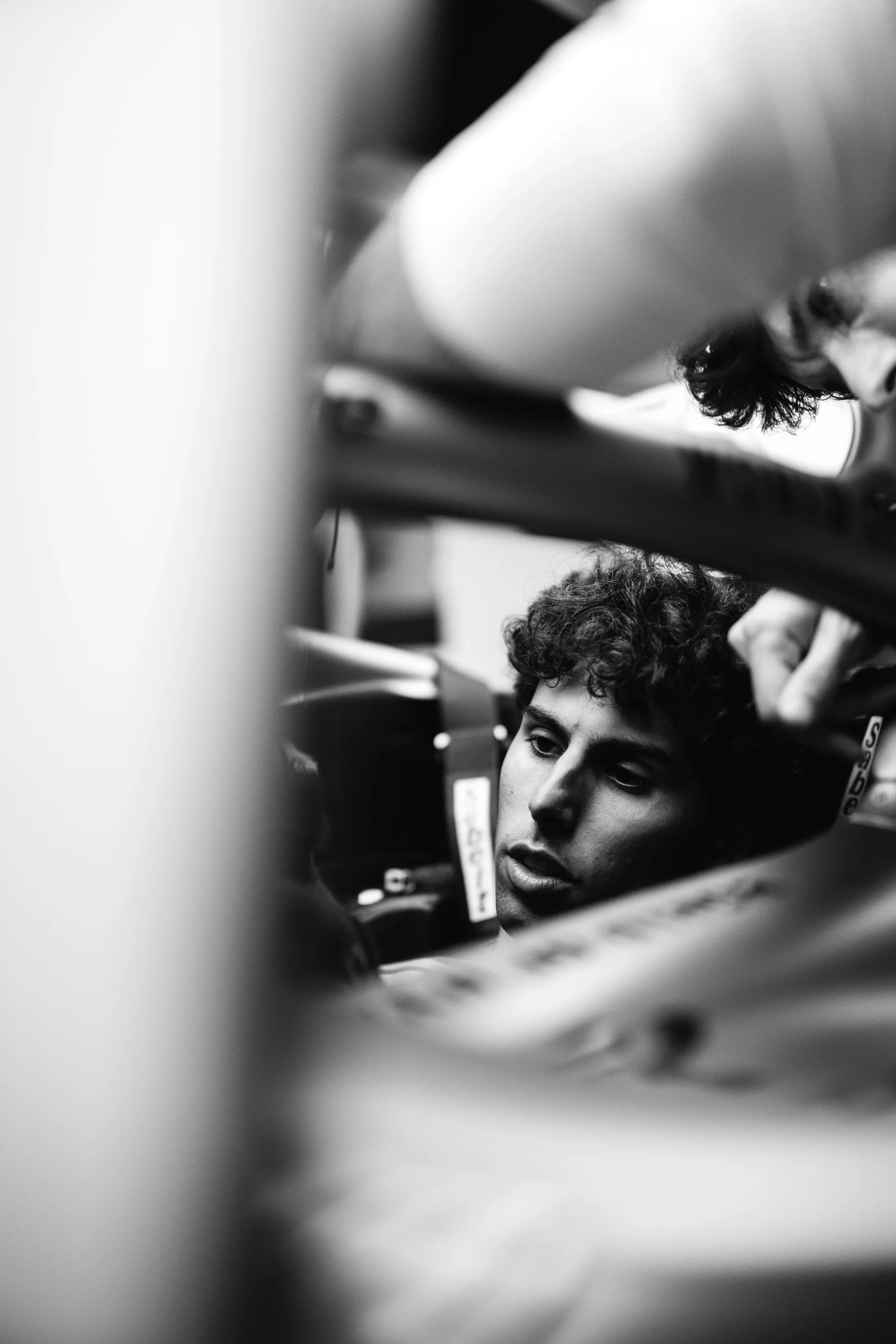 Black and white image ofGabriel Bortoleto seated in the cockpit during preparation, partially obscured by the car structure.