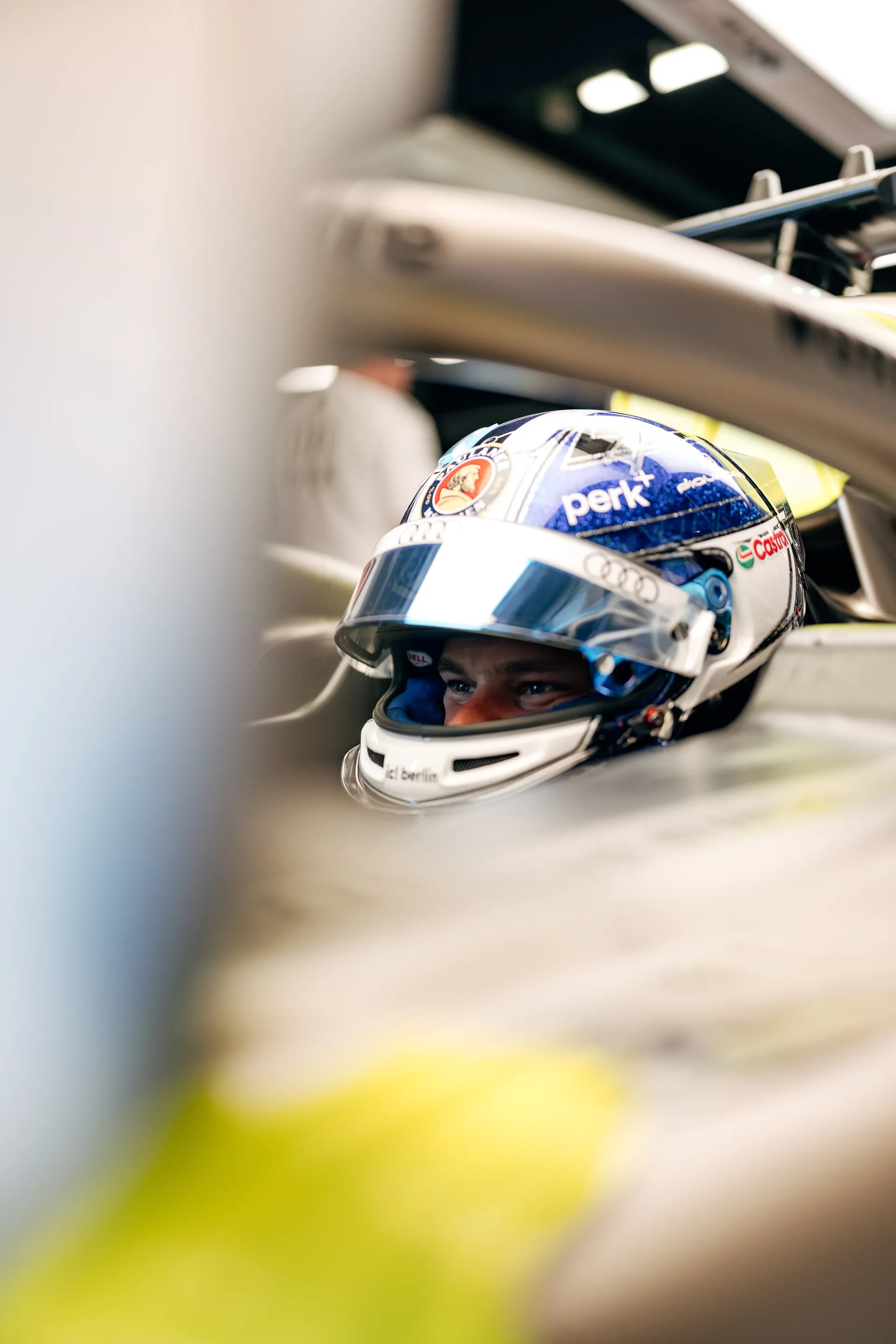 Tight cockpit shot of Paul Aron wearing a blue helmet, with team members assisting around the car.