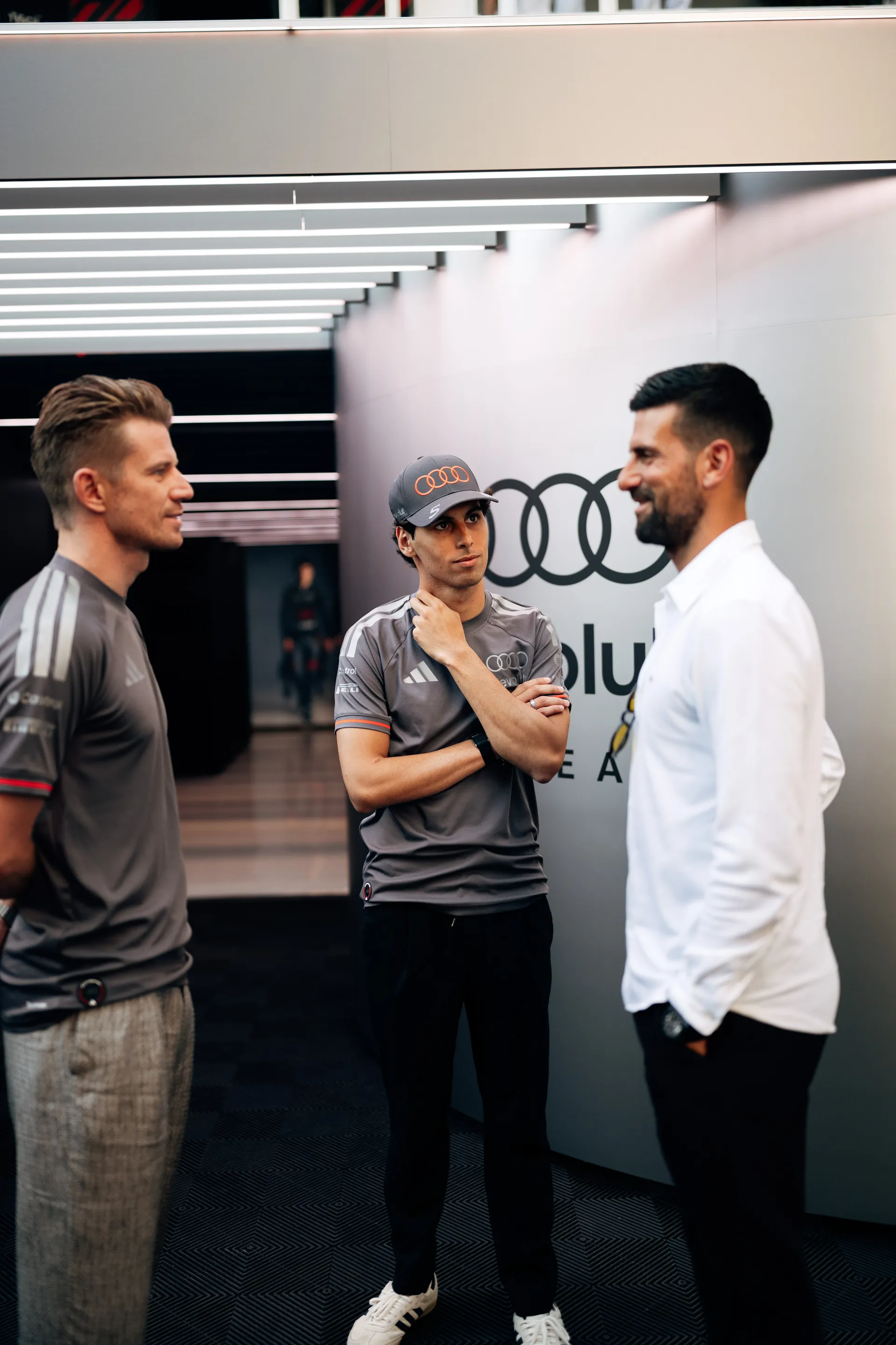Nico Hulkenberg, Gabriel Bortoleto and Novak Djokovic in conversation inside the Audi Revolut F1® Team garage
