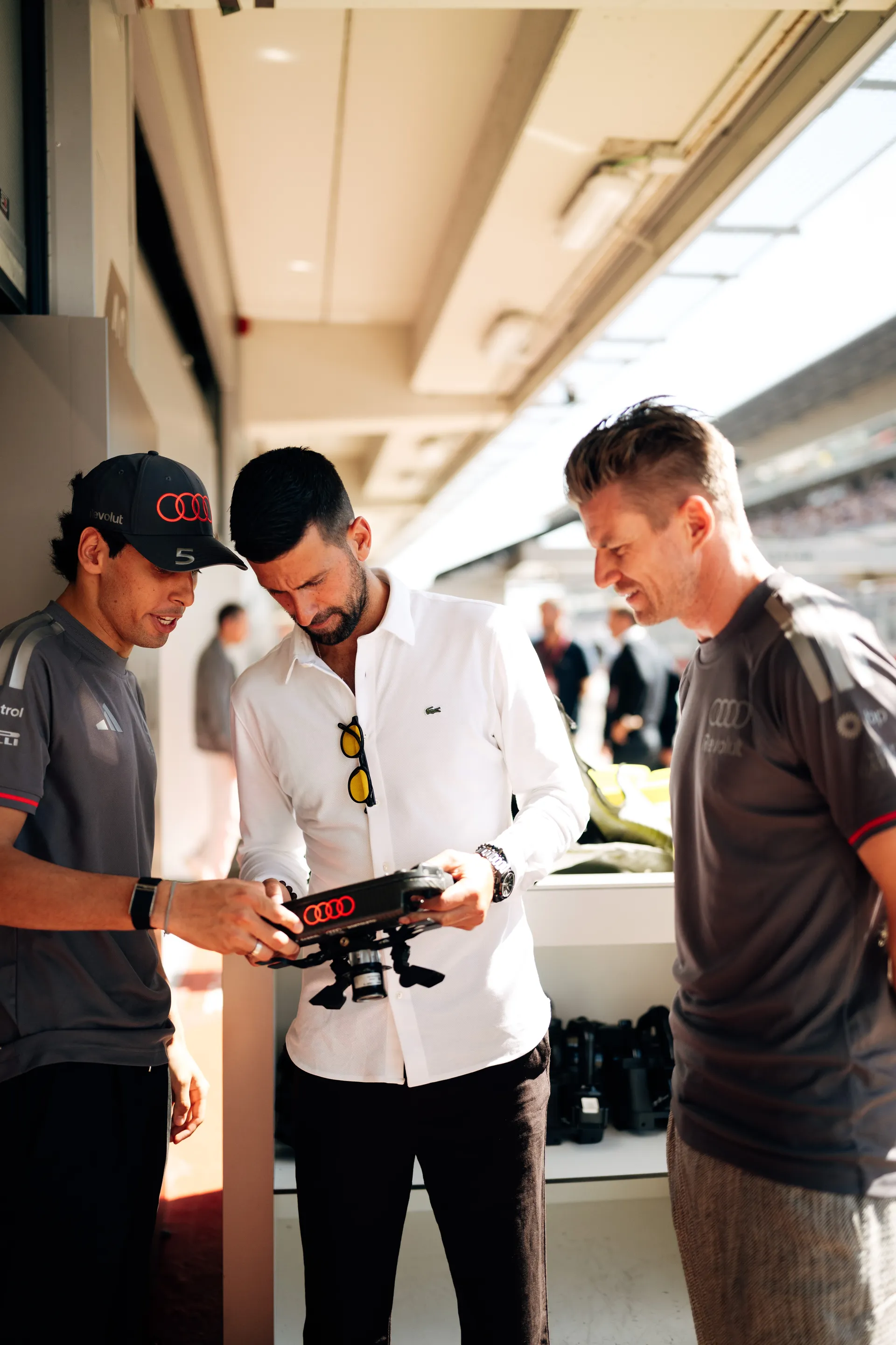 Nico Hulkenberg, Gabriel Bortoleto and Novak Djokovic examining the steering wheel together during the race weekend