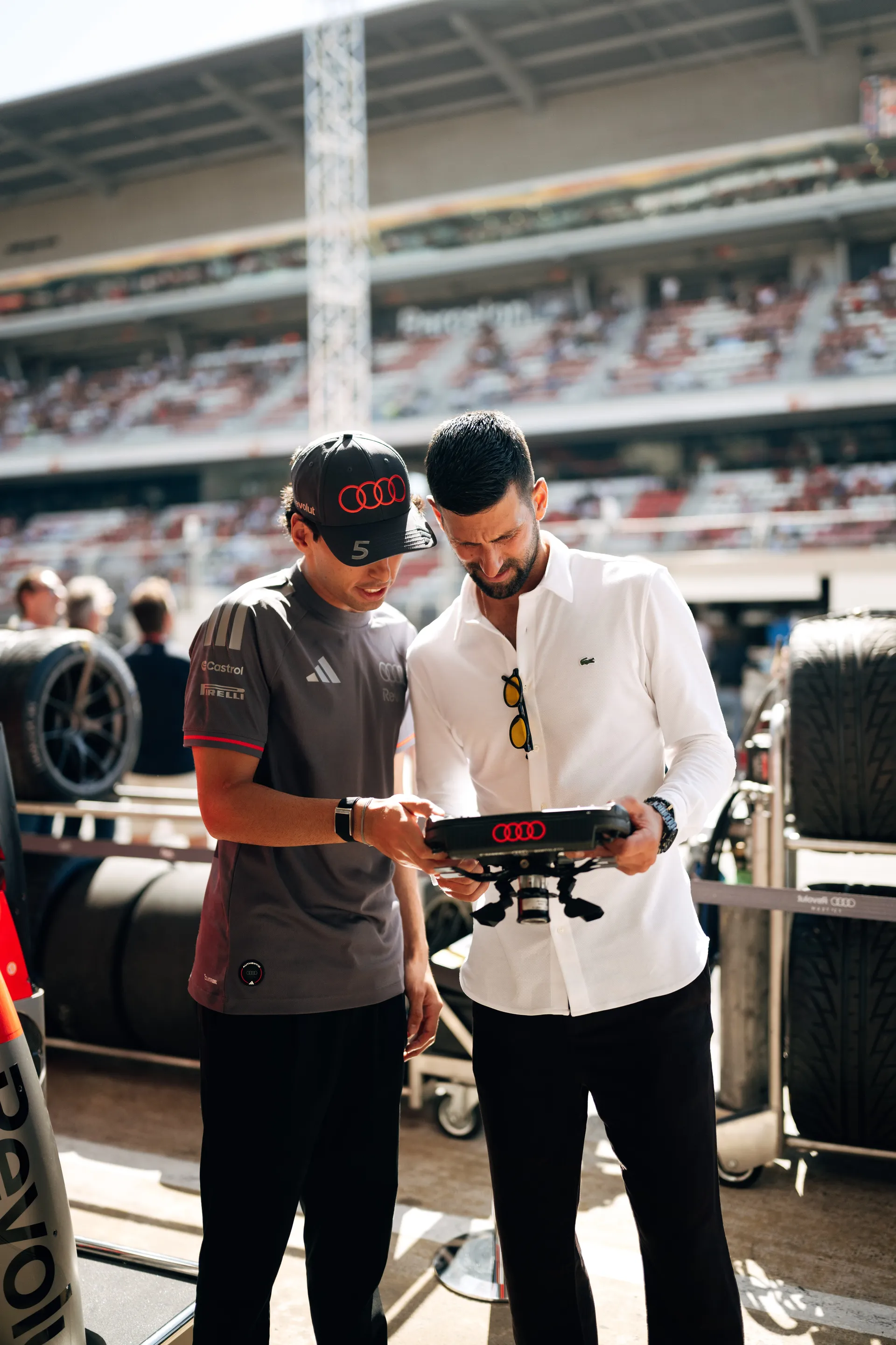 Close up of Gabriel Bortoleto explaining details of the steering wheel to Novak Djokovic