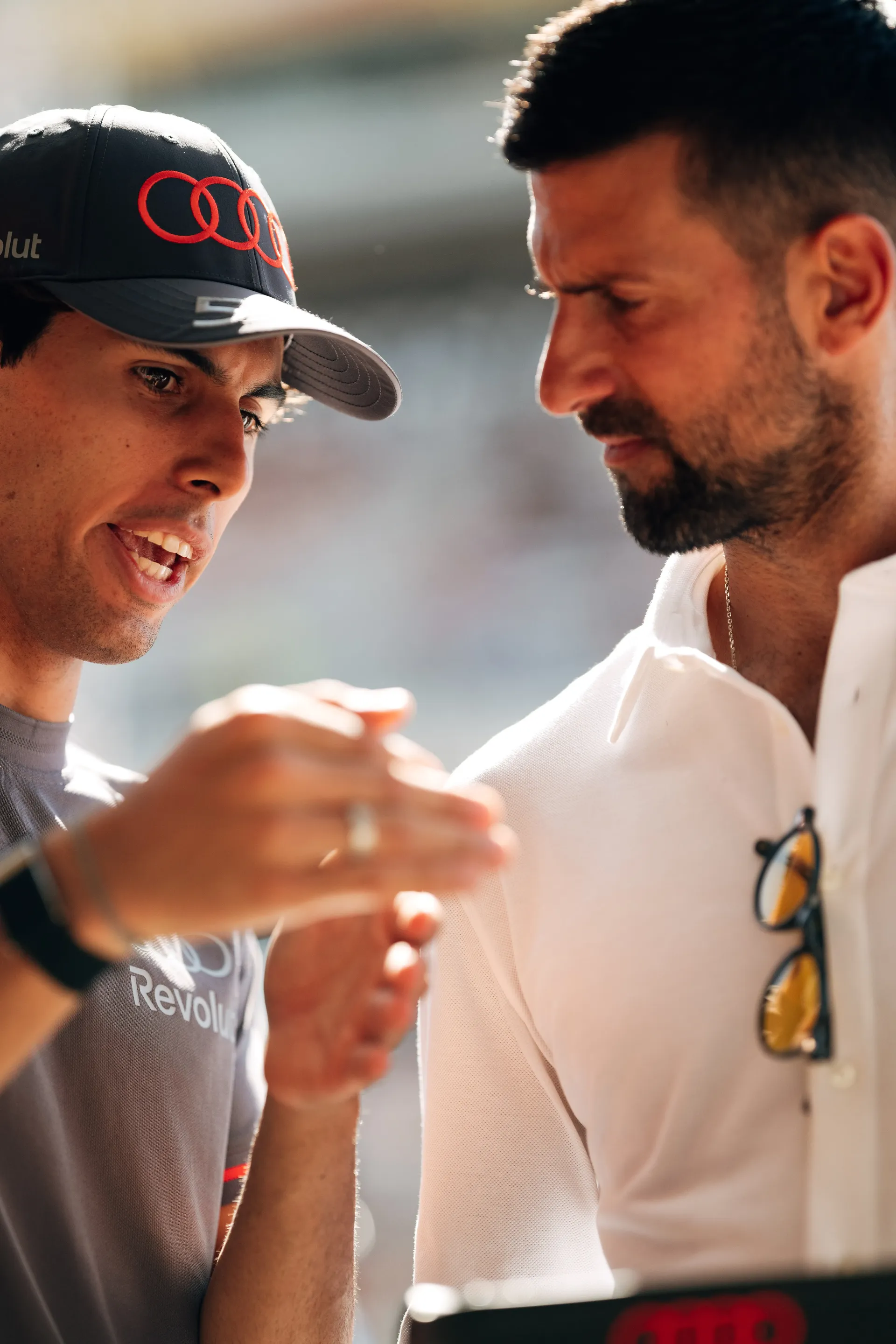 Close up of Gabriel Bortoleto explaining details of the steering wheel to Novak Djokovic