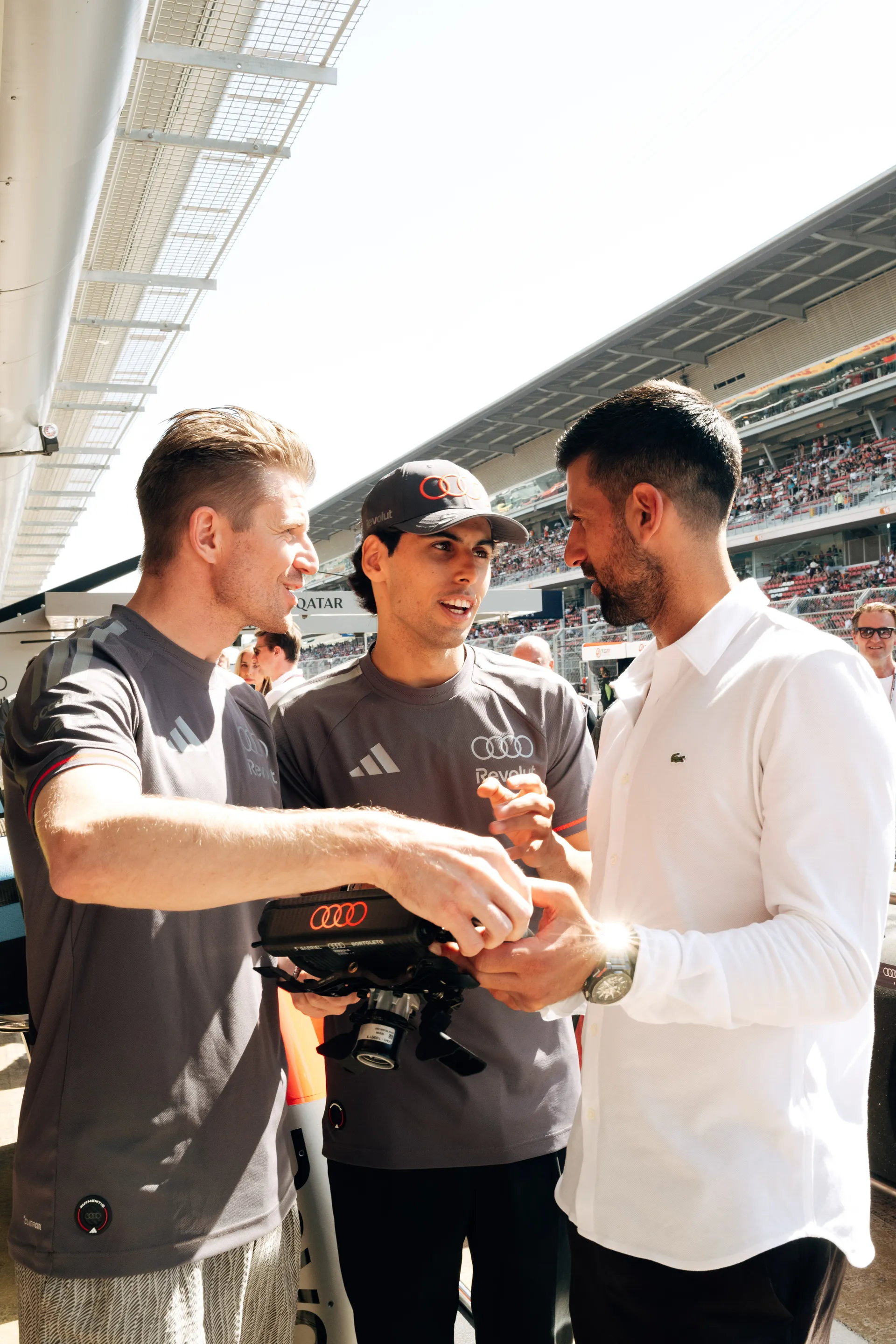 Nico Hulkenberg, Gabriel Bortoleto and Novak Djokovic examining the steering wheel together during the race weekend