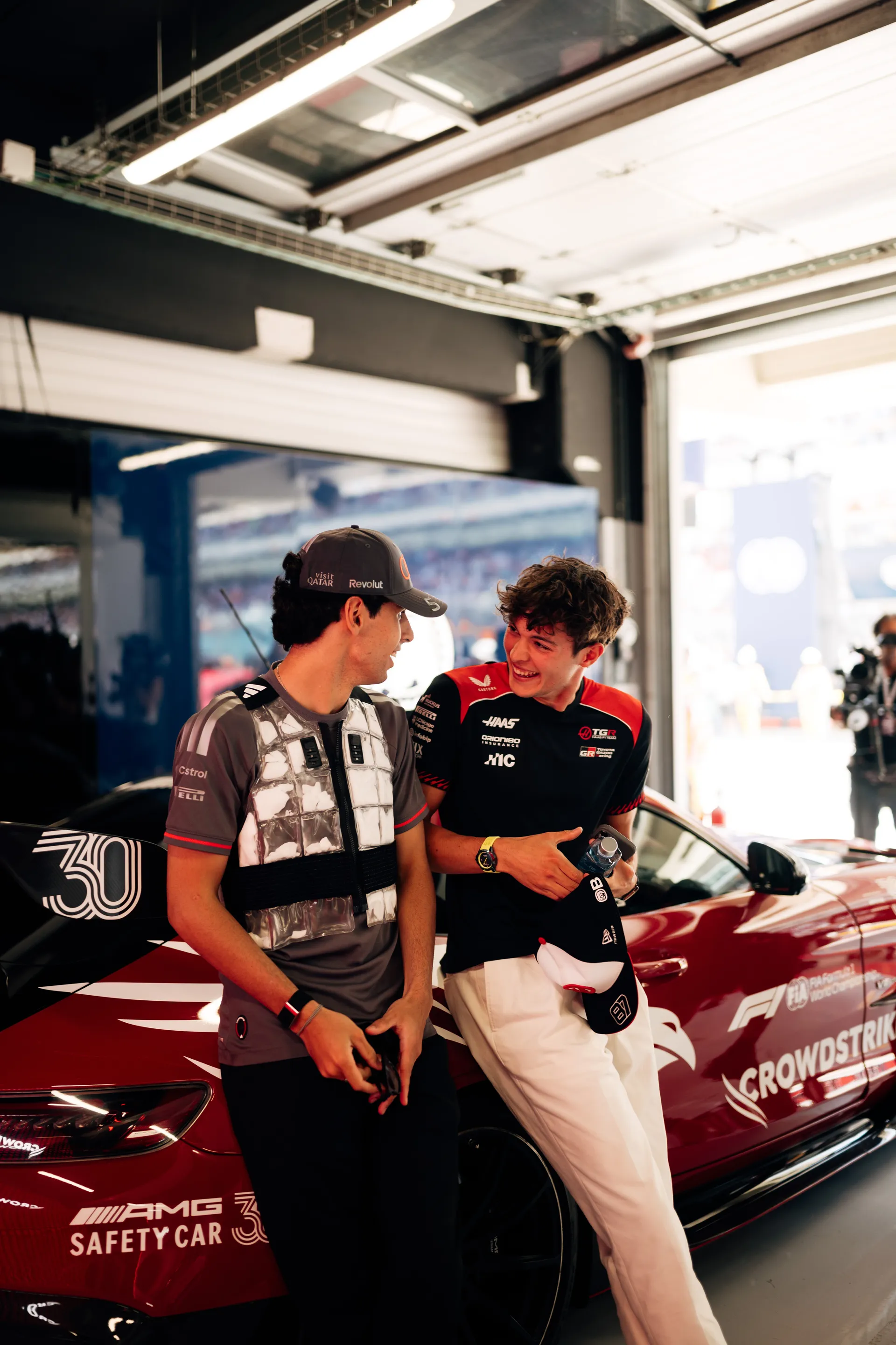 Gabriel Bortoleto and a fellow driver sharing a relaxed moment beside the Formula 1 safety car in the Audi Revolut F1® Team garage