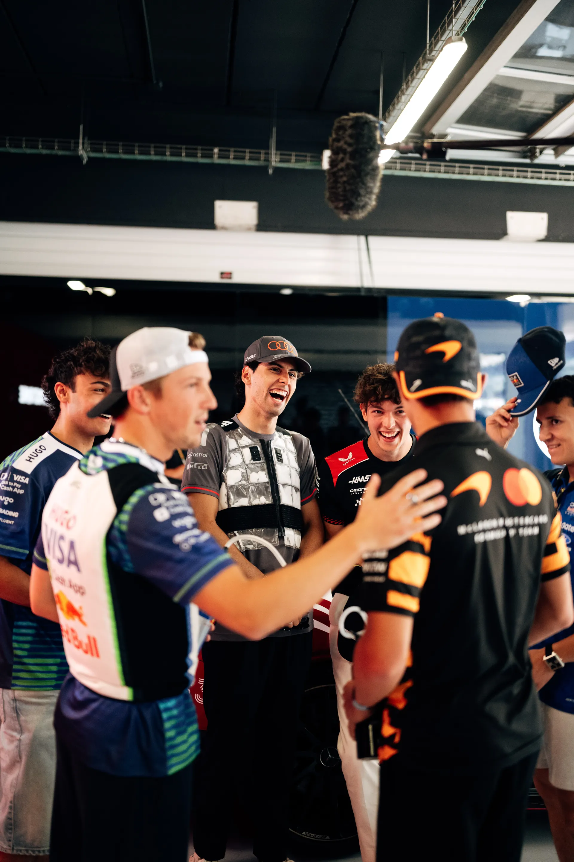 Gabriel Bortoleto interacting with multiple Formula 1 drivers in a group setting inside the garage during the Barcelona race weekend