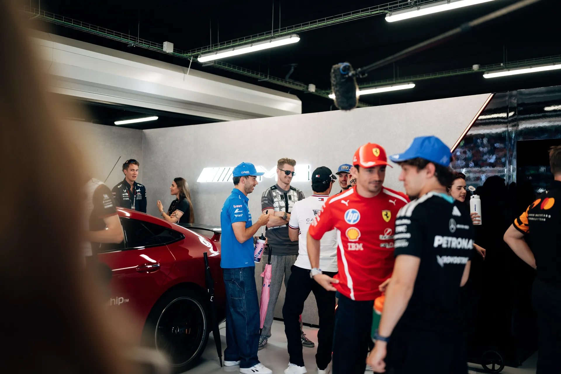 Nico Hulkenberg and multiple Formula 1 drivers gathered inside the Audi Revolut F1® Team garage, including Ferrari and Mercedes drivers, engaging in casual conversation near the safety car