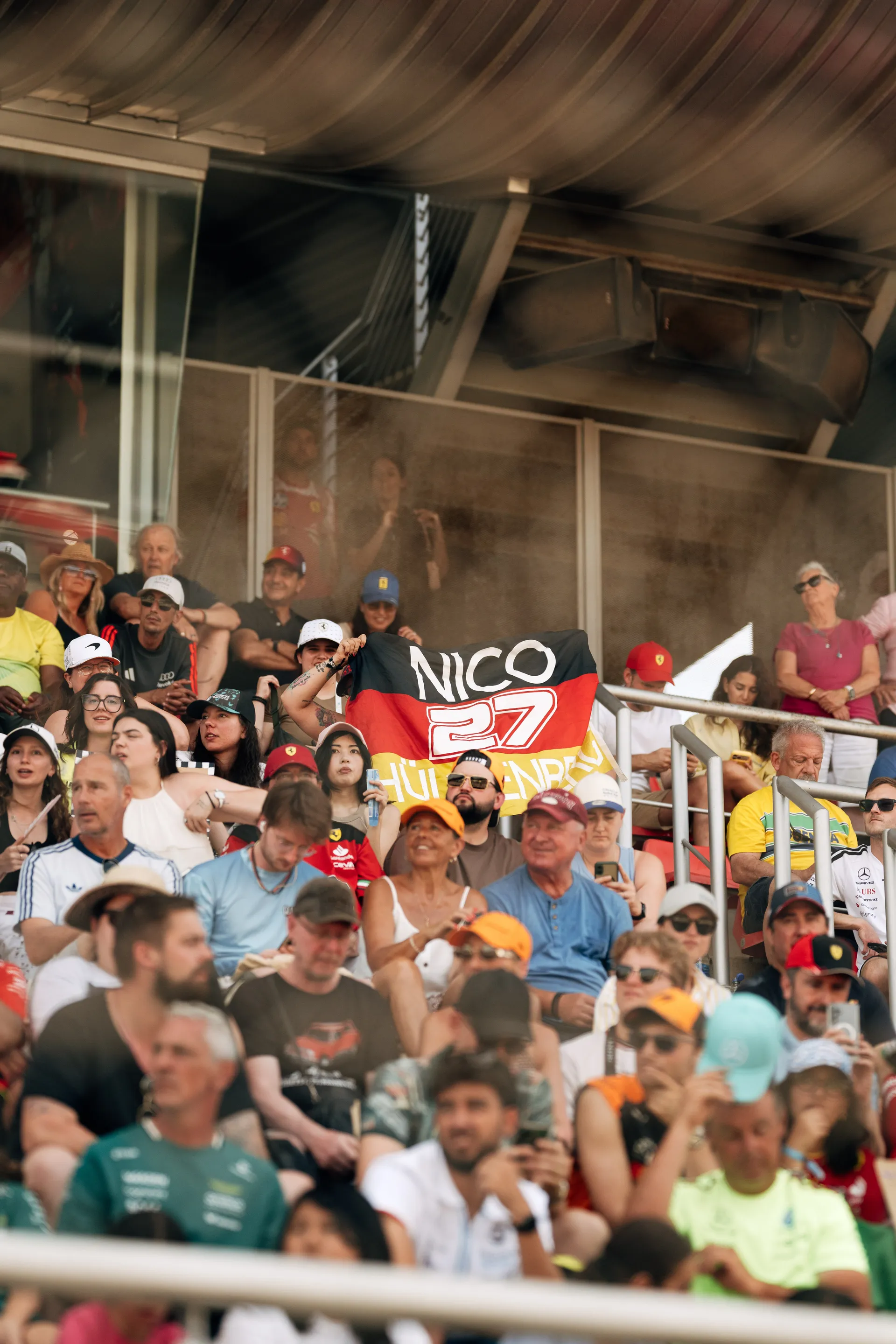 Grandstand crowd at the Barcelona Grand Prix with a fan holding a German flag reading “NICO 27” in support of Nico Hulkenberg