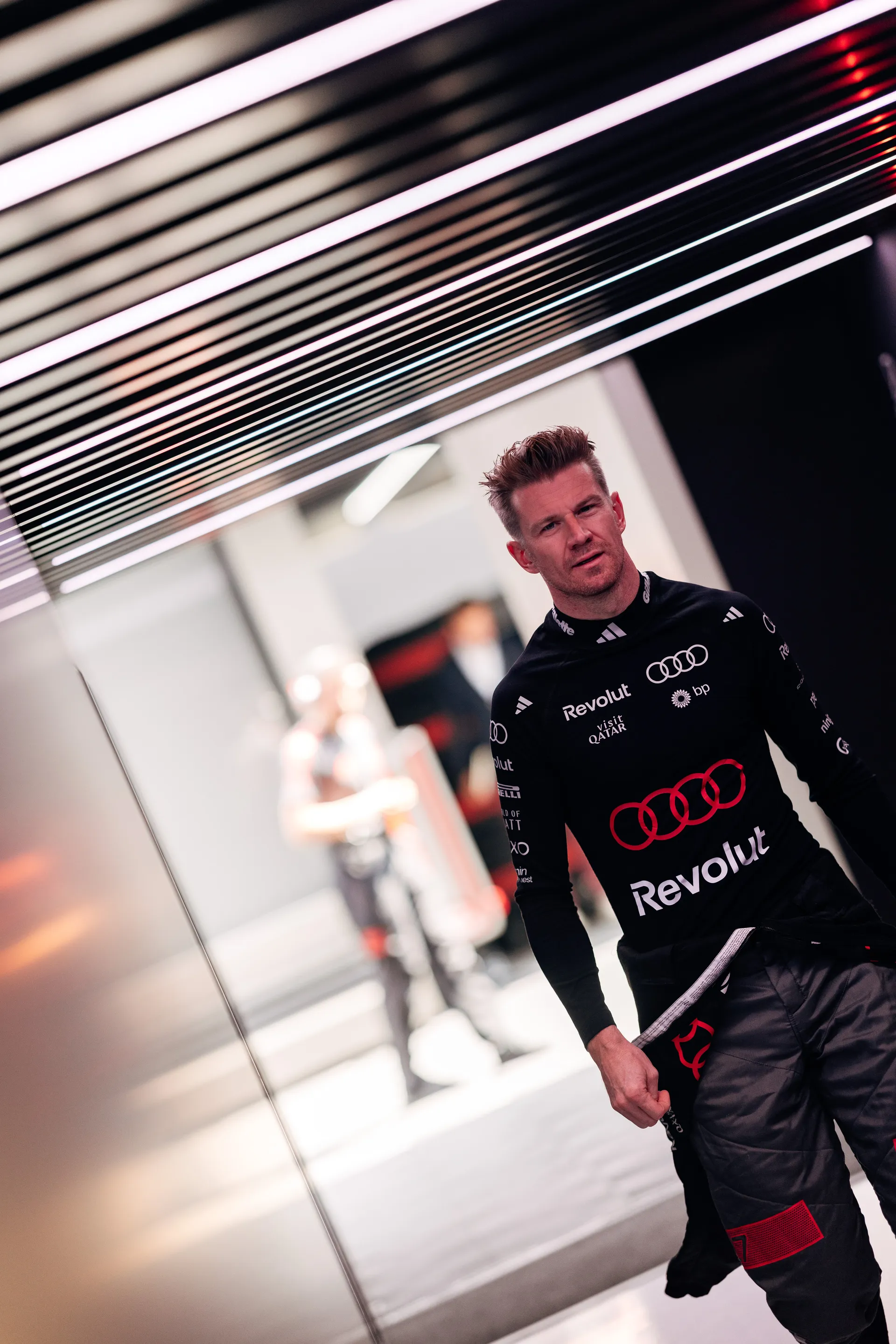 Nico Hulkenberg walks through the Audi Revolut F1® Team garage corridor in race suit, heading towards the pit area during the Belgian Grand Prix weekend.