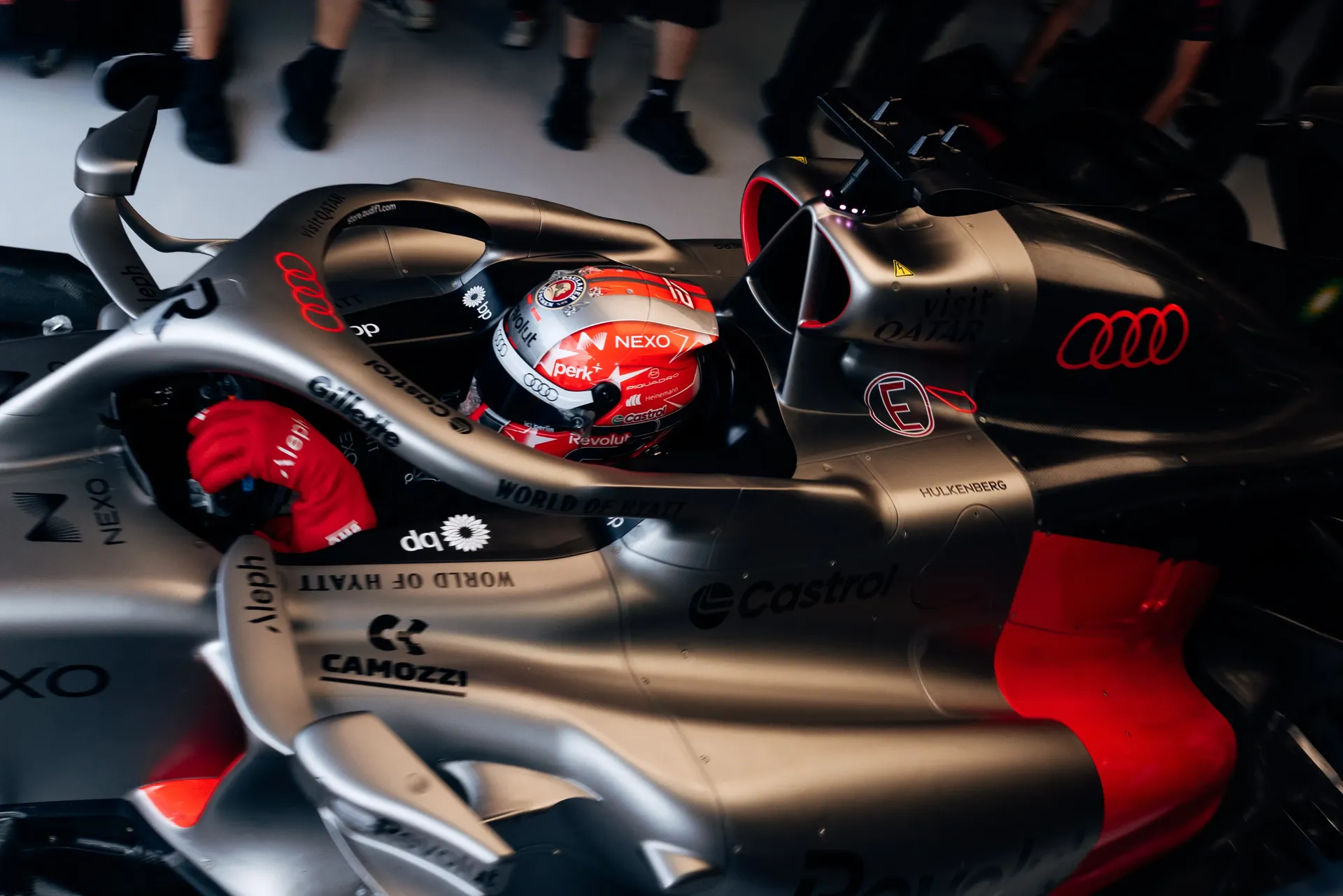 Nico Hulkenberg sits in the Audi Revolut F1® Team car as mechanics prepare the car in the garage.