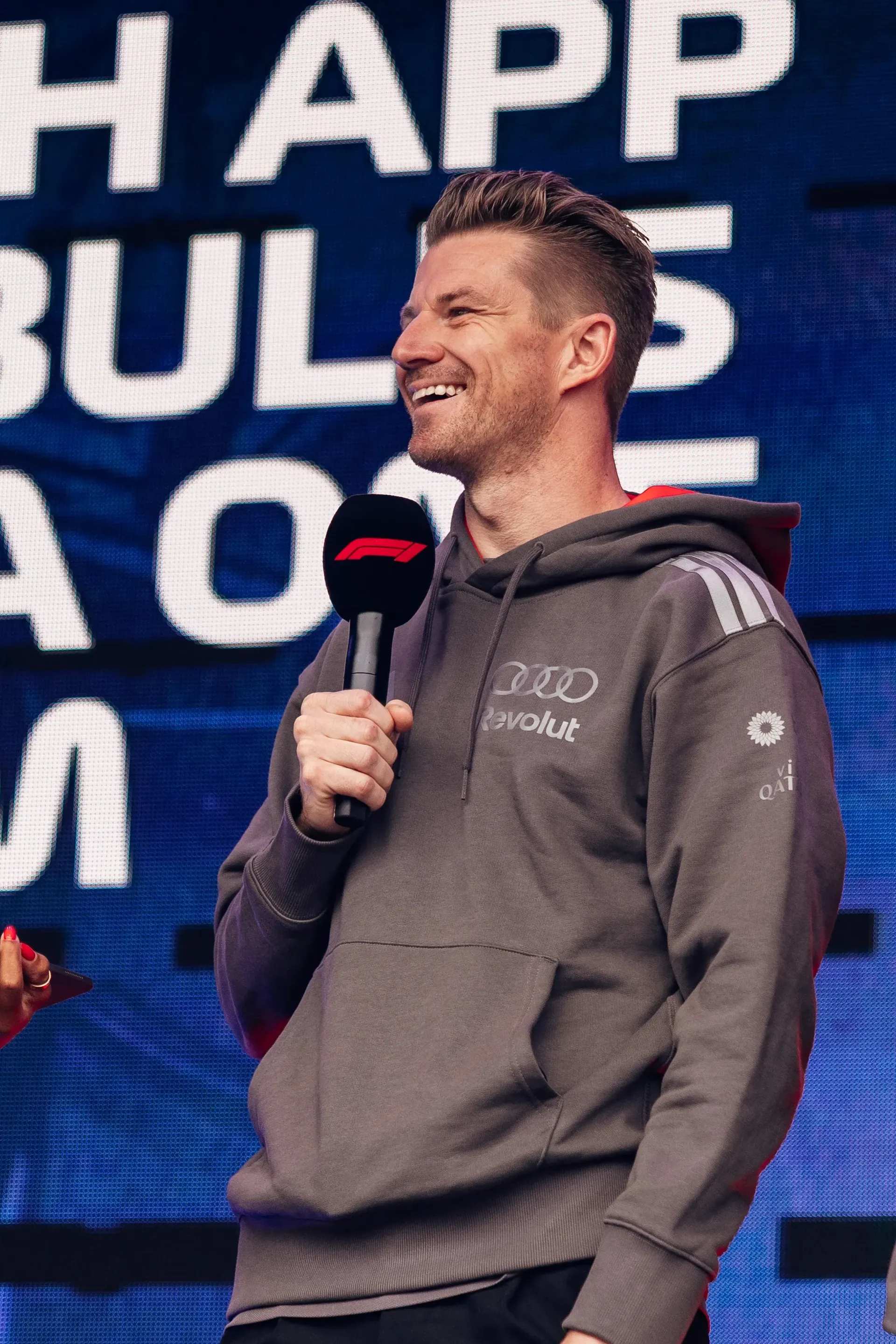 Nico Hulkenberg speaks on stage during the Belgian Grand Prix fan forum, holding a microphone and wearing Audi Revolut F1® Team apparel.