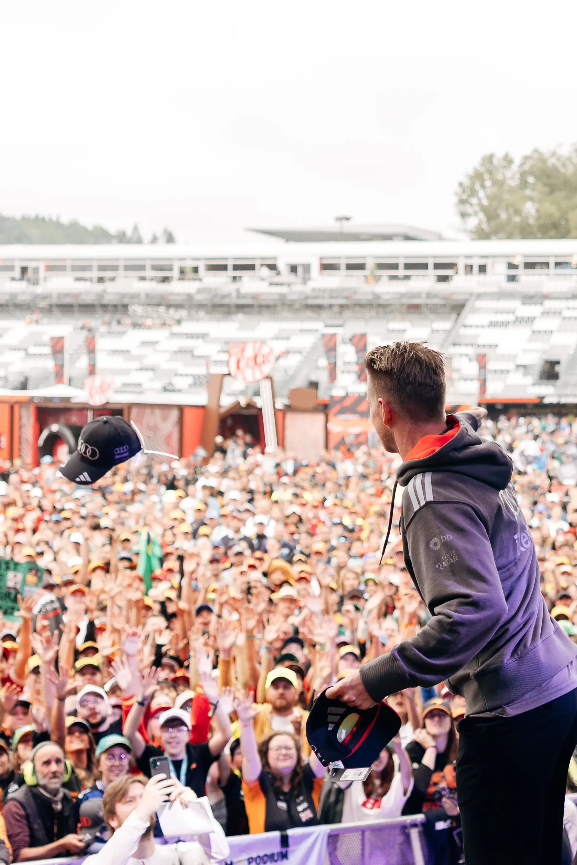 Nico Hulkenberg throws a cap into the crowd during the Belgian Grand Prix fan forum, with fans reaching up from the front rows.