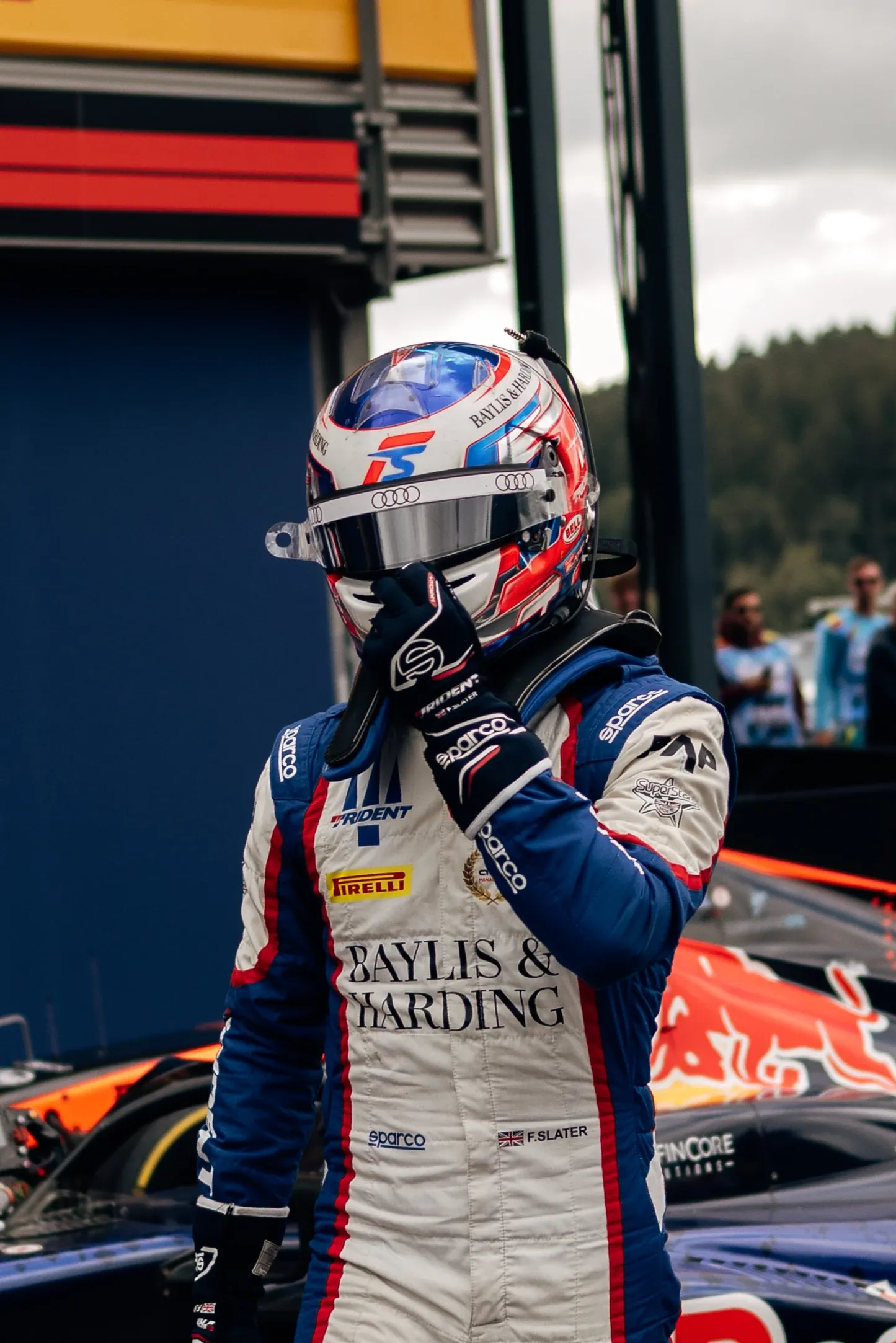 Freddie Slater adjusts his helmet on the grid at Spa Francorchamps standing next to his Formula 3 car after the race