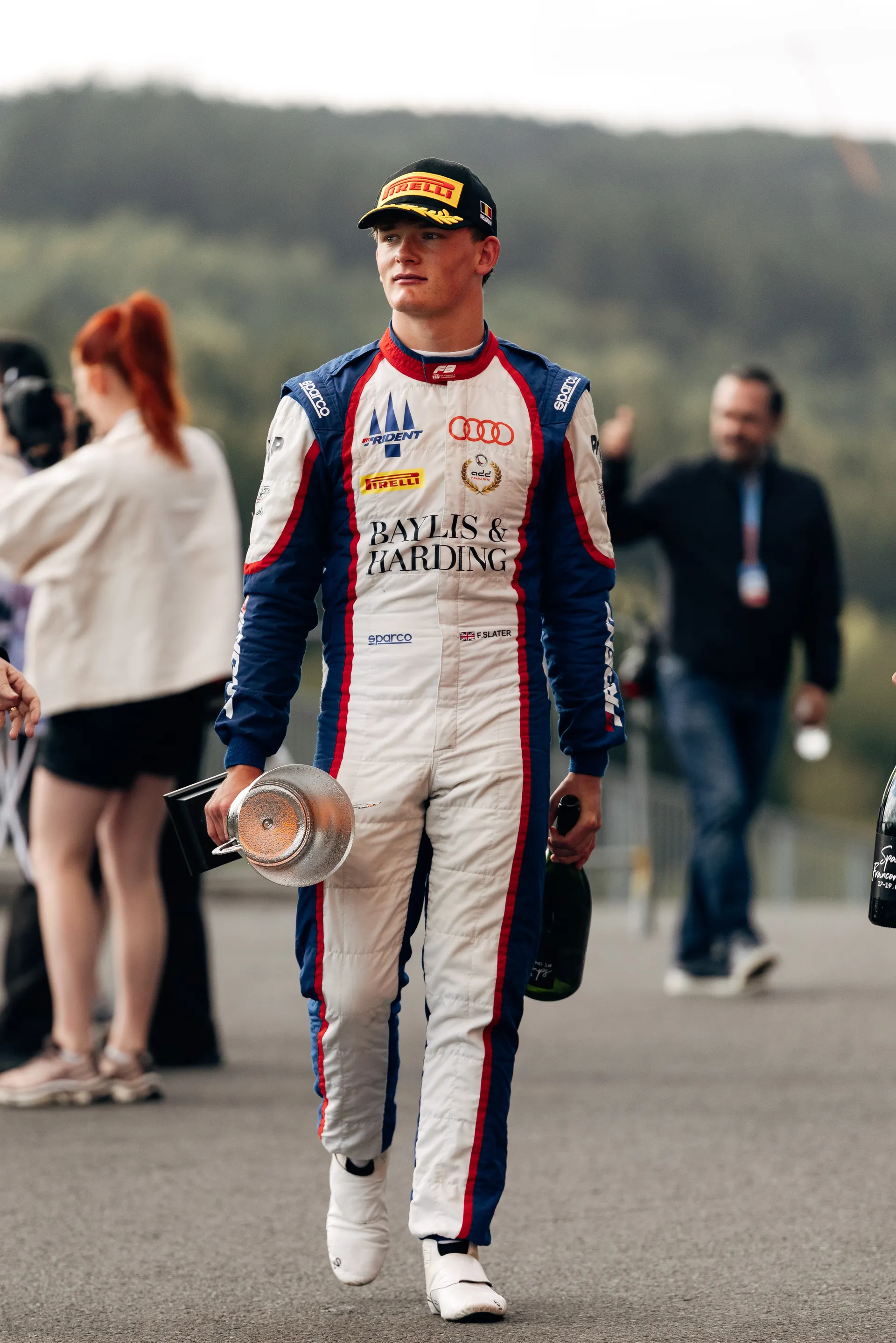 Freddie Slater walks through the paddock holding his trophy and champagne bottle after achieving P3 at Spa Francorchamps