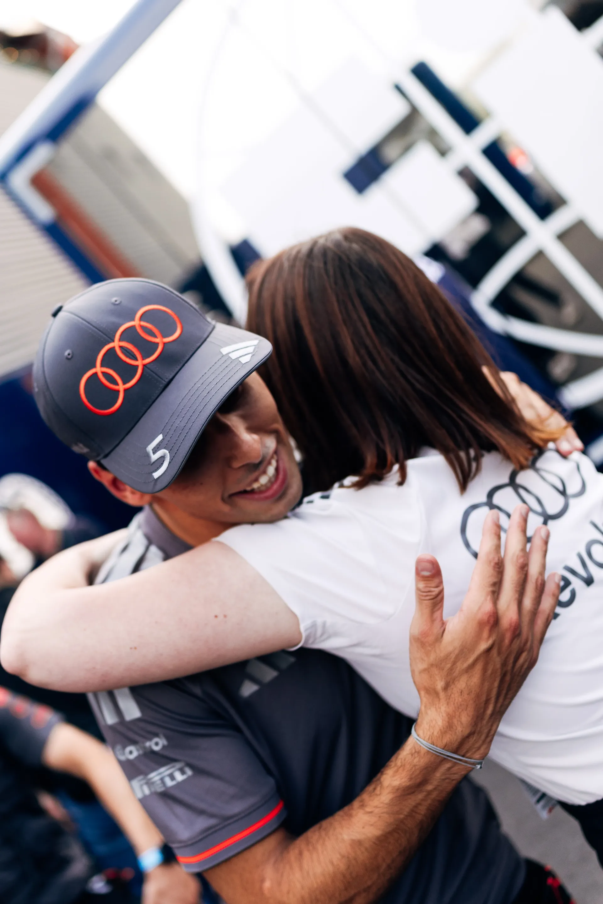 Gabriel Bortoleto greets a team member with a hug in the paddock, wearing Audi Revolut F1® Team cap and race kit after qualifying