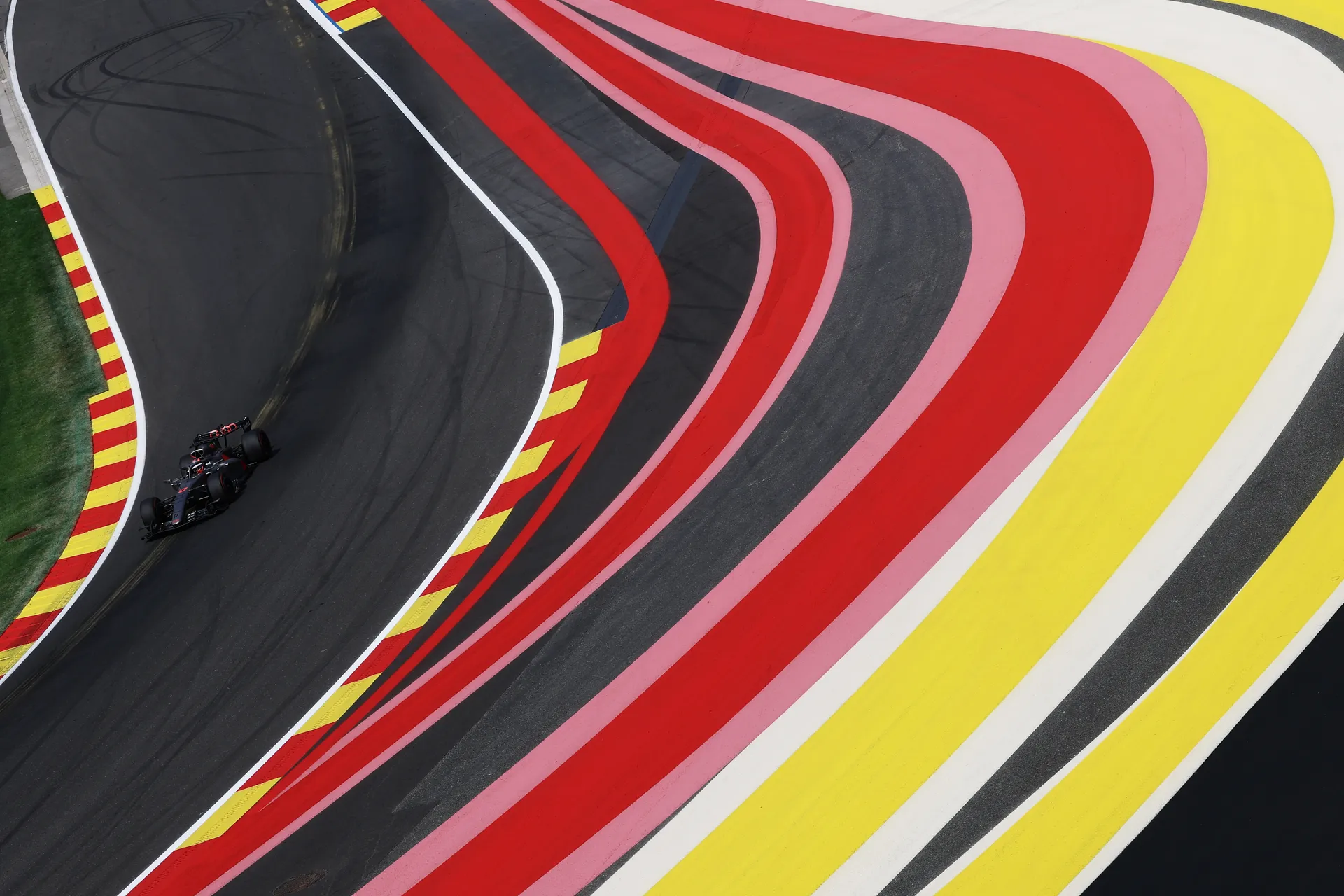 Overhead view of a Formula 1 car navigating a corner at Spa Francorchamps during qualifying, with bold red, yellow and white run off areas framing the track