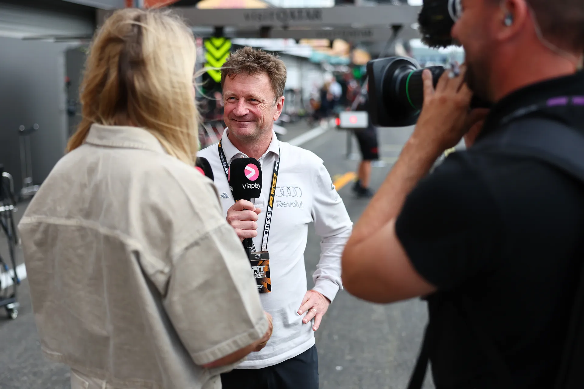 Allan McNish of Audi Revolut F1® Team smiling during a trackside interview while a cameraman films the conversation in the paddock