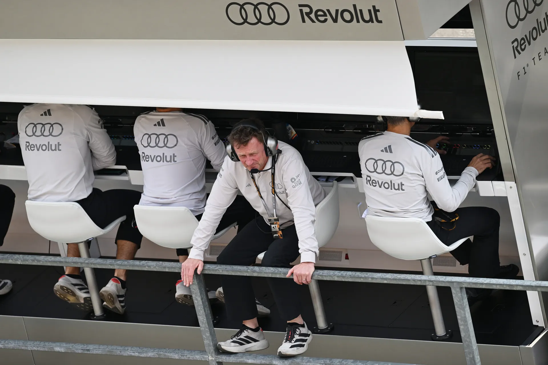 Allan McNish of Audi Revolut F1® Team leaning forward on the pit wall while monitoring qualifying alongside team members on the strategy stand