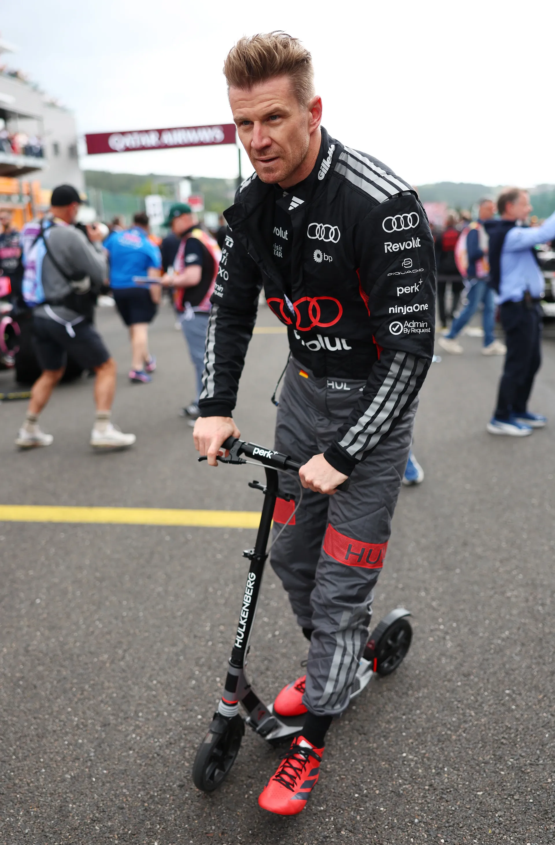 Nico Hulkenberg rides a scooter through the paddock in his Audi Revolut F1® Team race suit at Spa-Francorchamps.