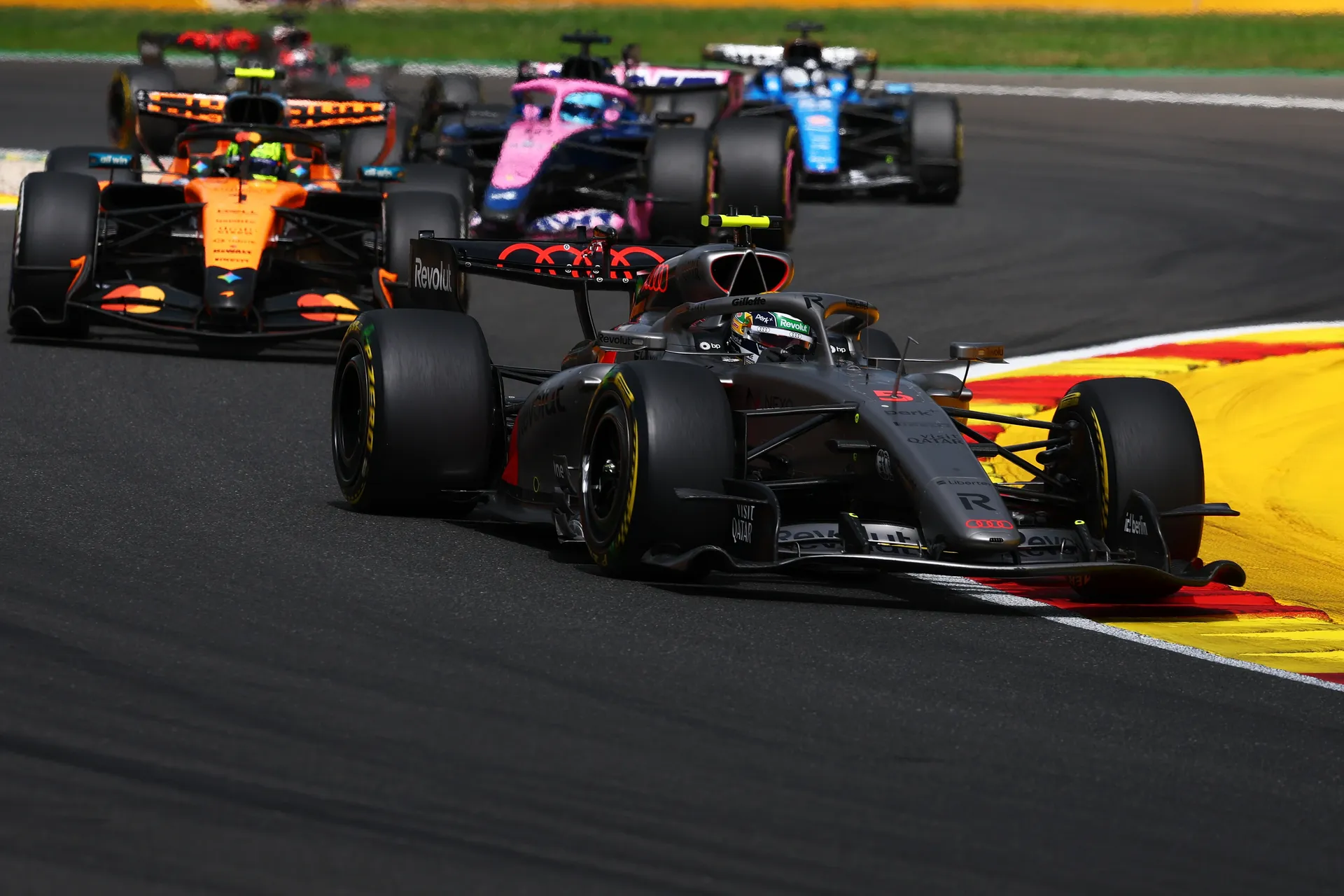 The Audi R26 leads a group of Formula One cars through a corner, holding position under pressure at Spa-Francorchamps.