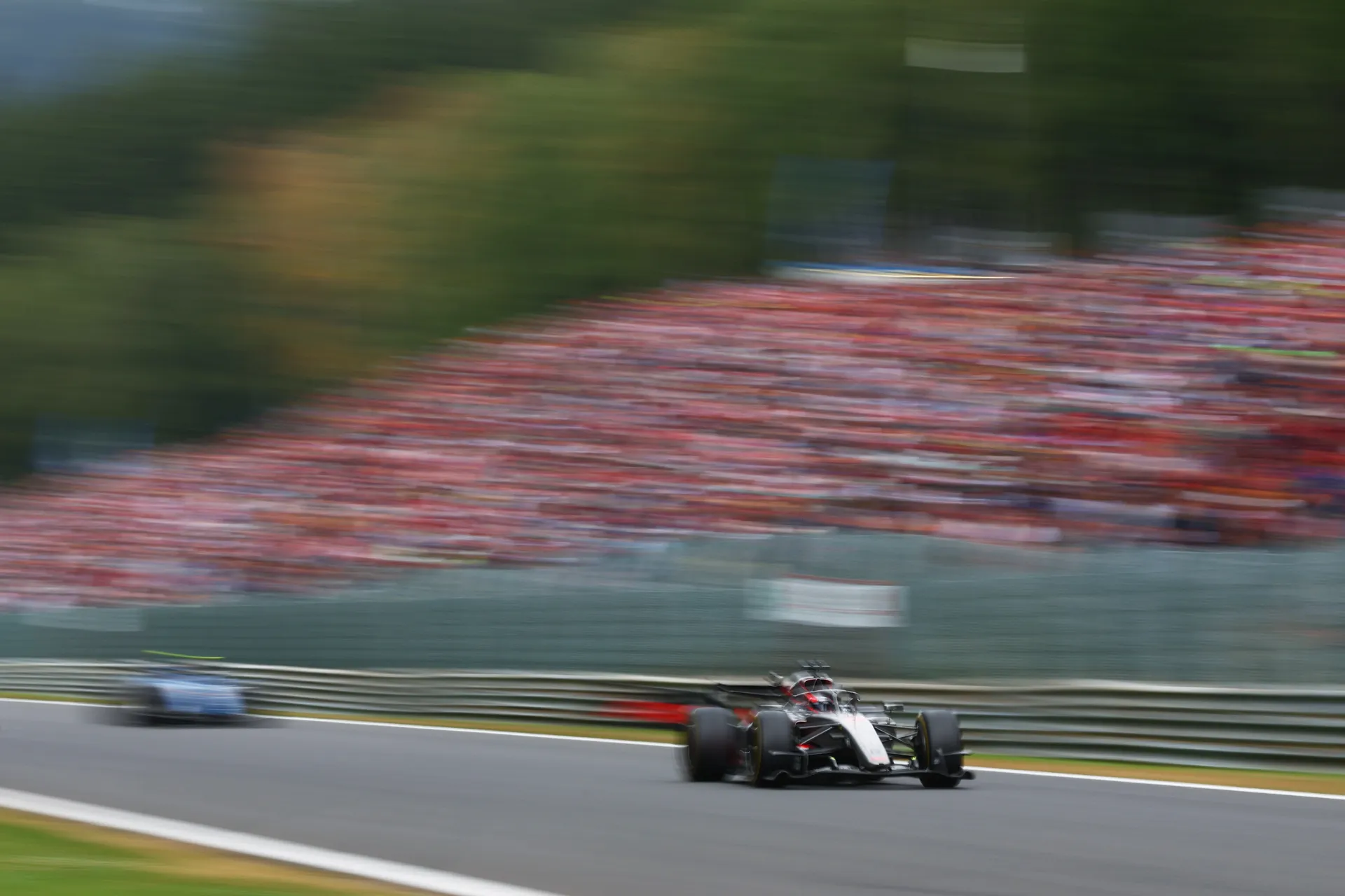 The Audi R26 races through the Ardennes with the grandstands blurred in the background, capturing the speed of Spa.
