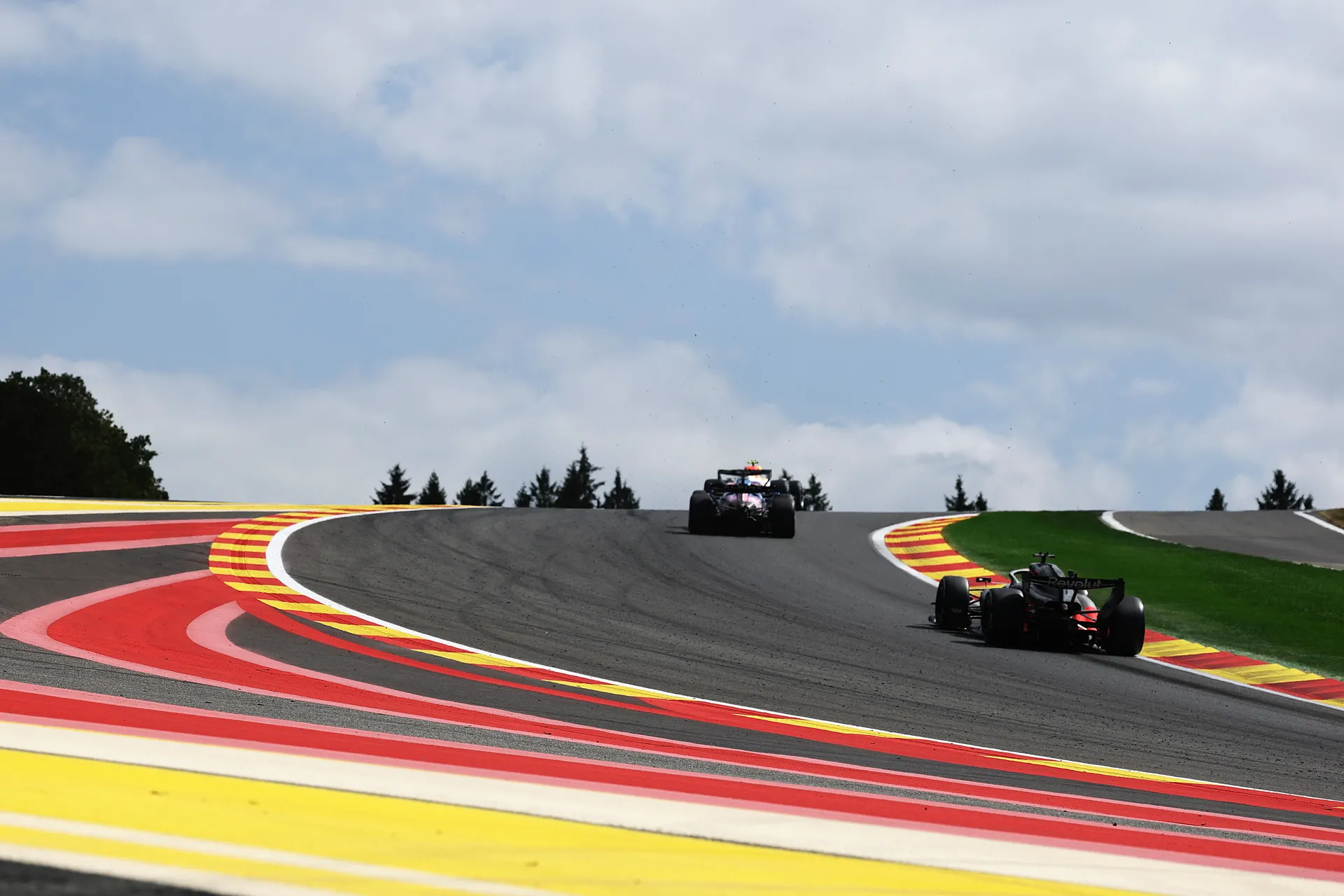 Two Formula One cars crest Eau Rouge and Raidillon, highlighting the elevation change at Spa-Francorchamps.