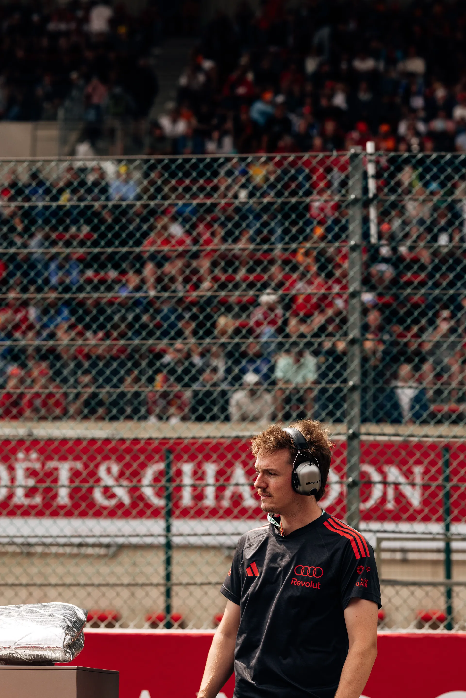 Audi Revolut F1® Team crew member wearing headset monitors trackside activity in front of grandstands at Spa-Francorchamps.