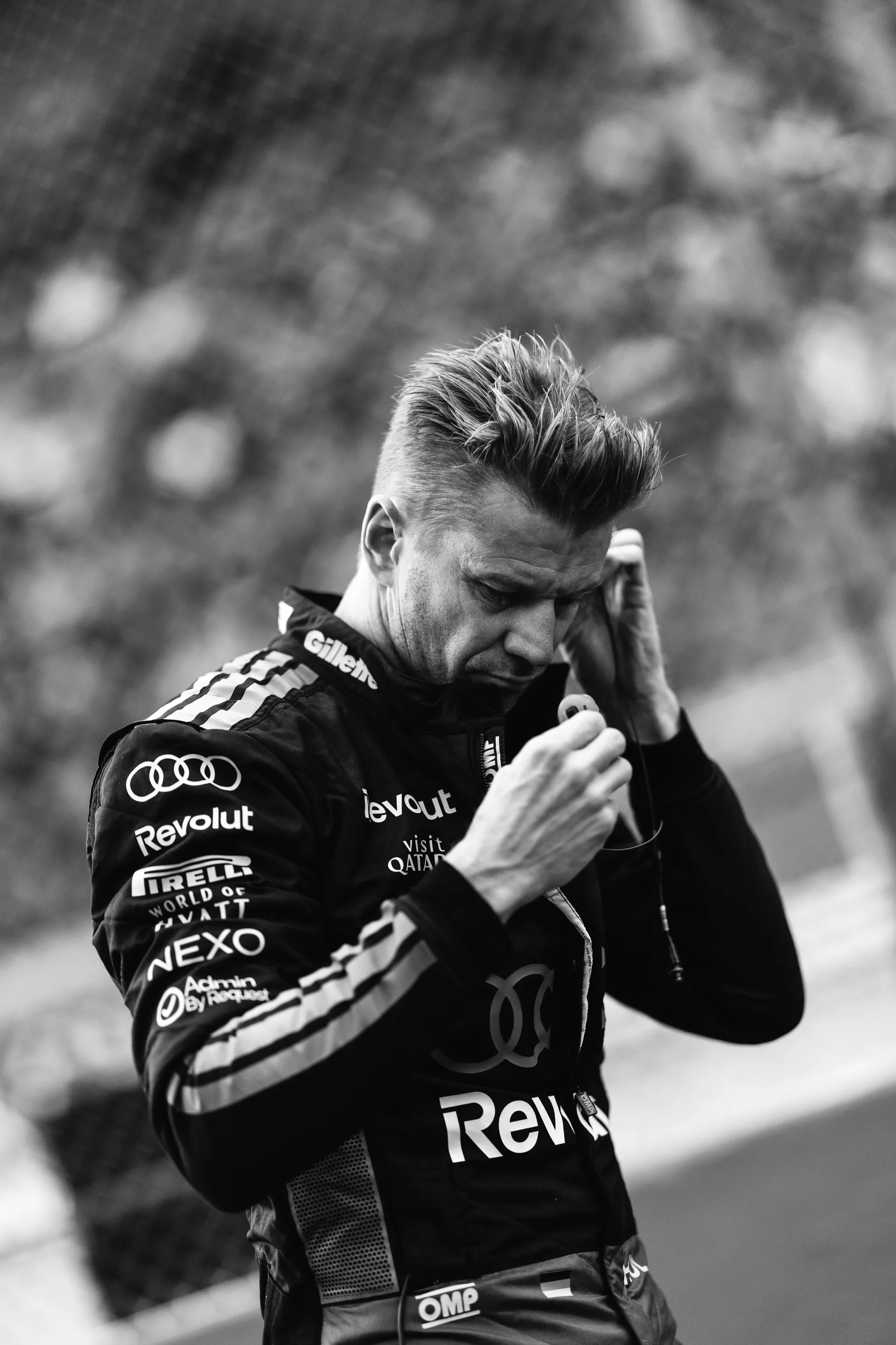 Nico Hulkenberg adjusts his earpiece while wearing Audi Revolut F1® Team race suit in a black-and-white portrait at Spa-Francorchamps.