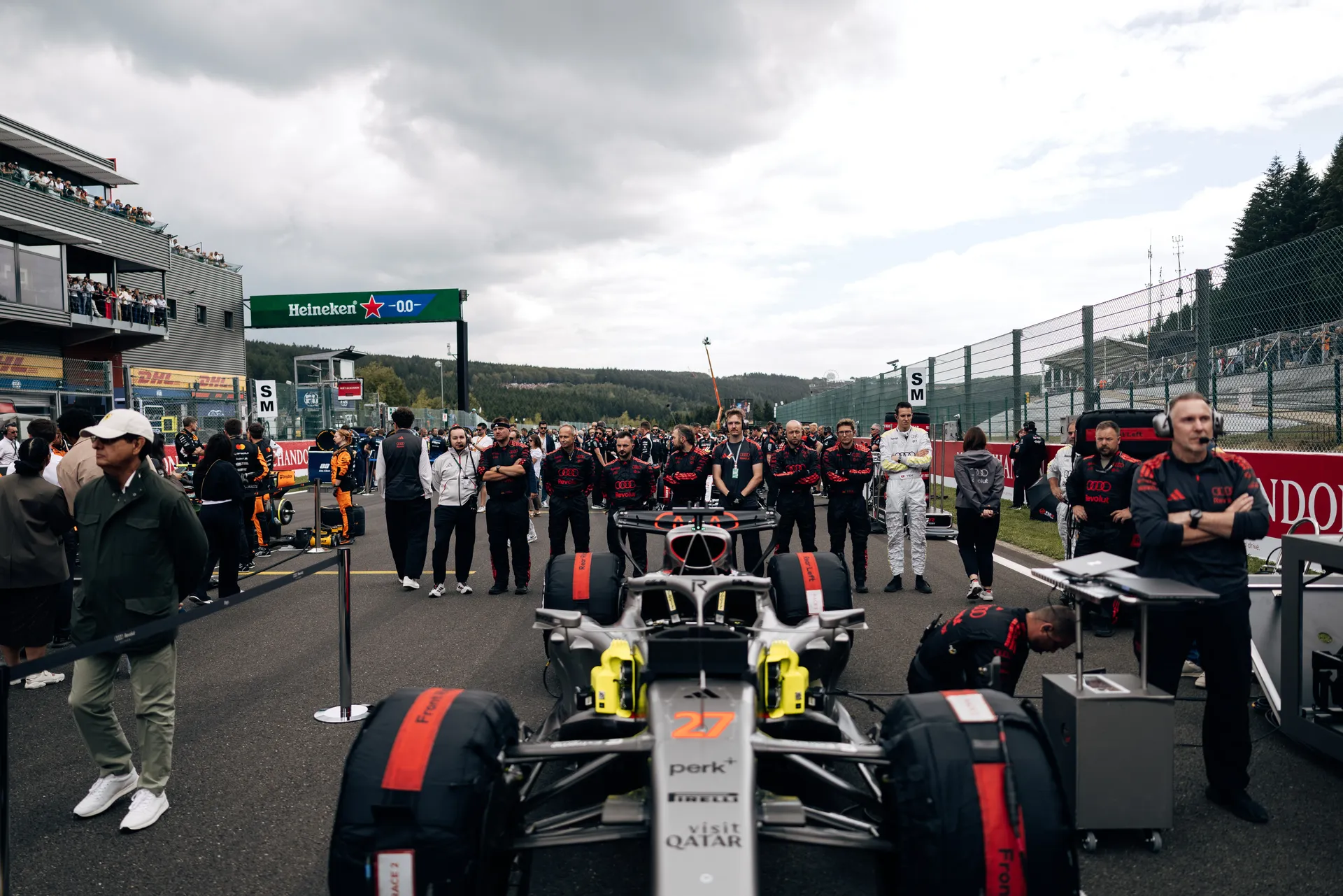 Front view of an Audi Revolut F1® Team R26 positioned on the Spa-Francorchamps starting grid, surrounded by team members and race crews before the start