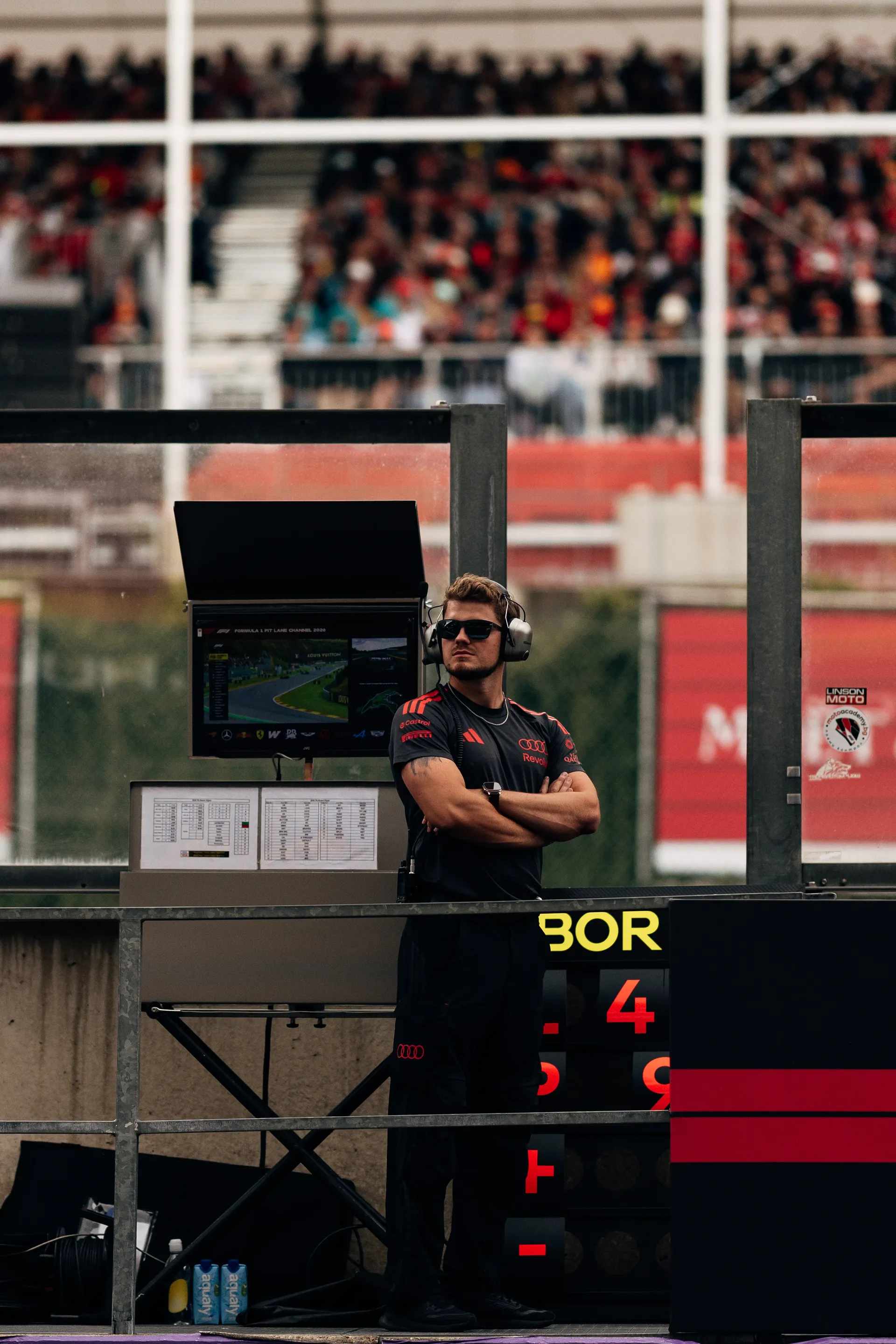 Audi Revolut F1® Team crew member wearing a headset stands on the pit wall monitoring race data screens with grandstands full of spectators behind