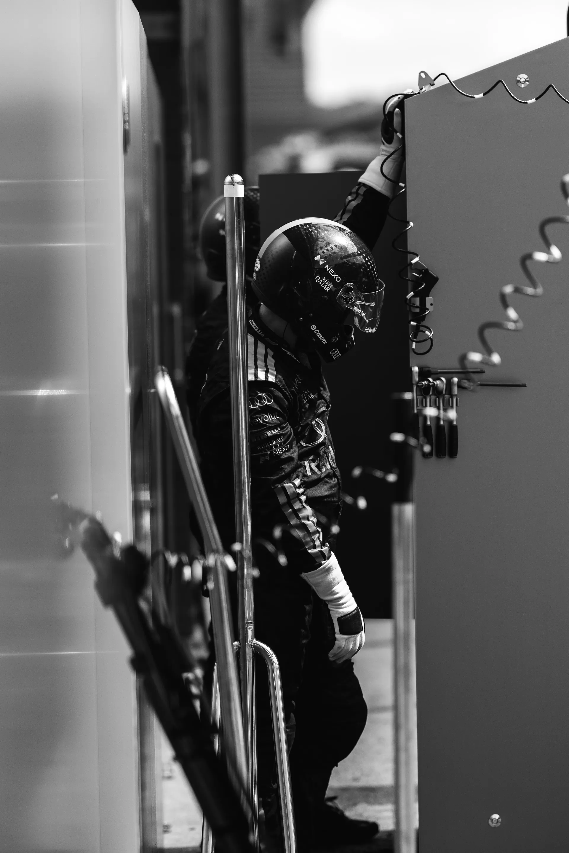 Audi Revolut F1® Team pit crew member in helmet stands beside garage equipment, reaching upward to adjust a cable