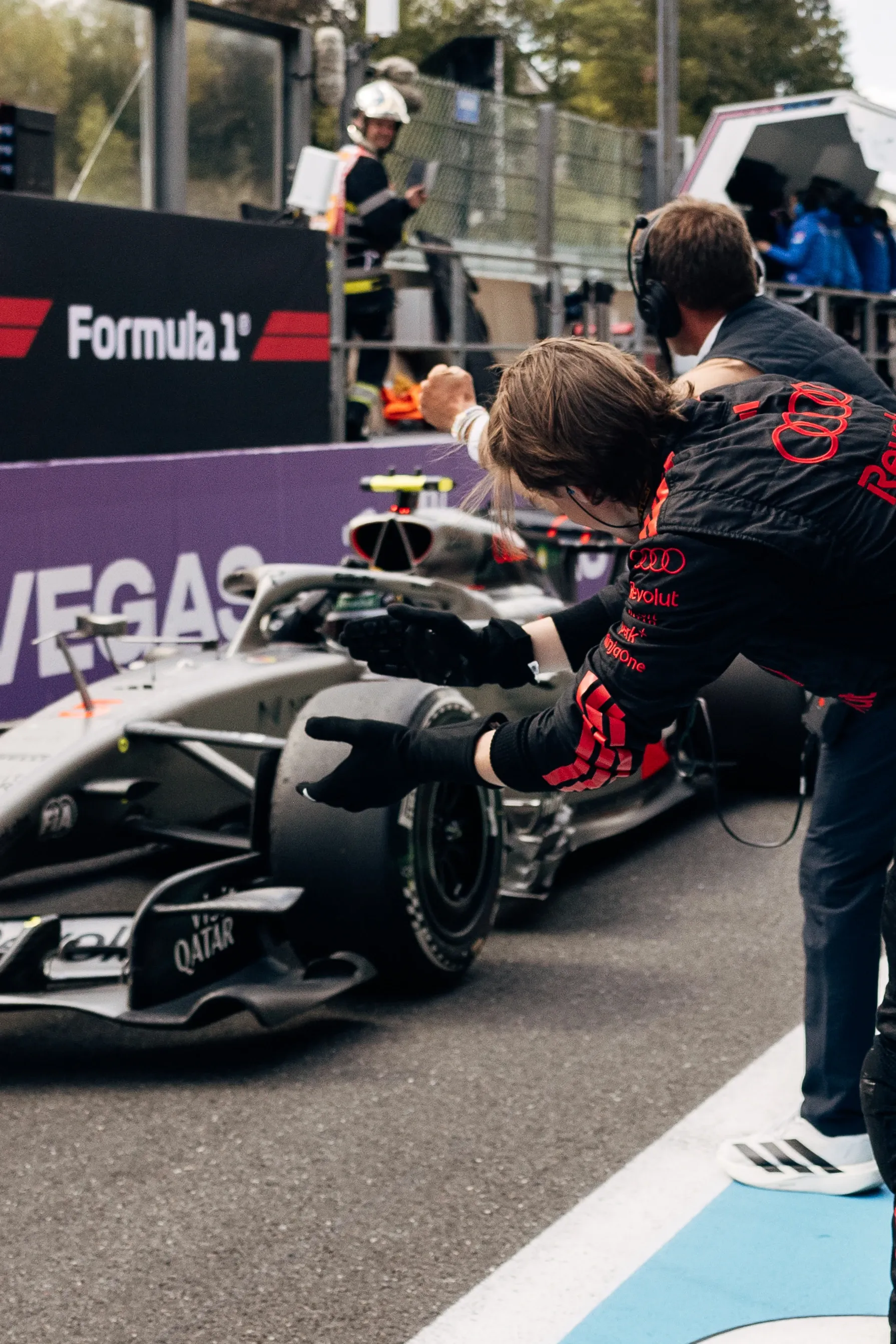 Audi Revolut F1® Team member embracing another person in the paddock area with team activity and spectators in the background