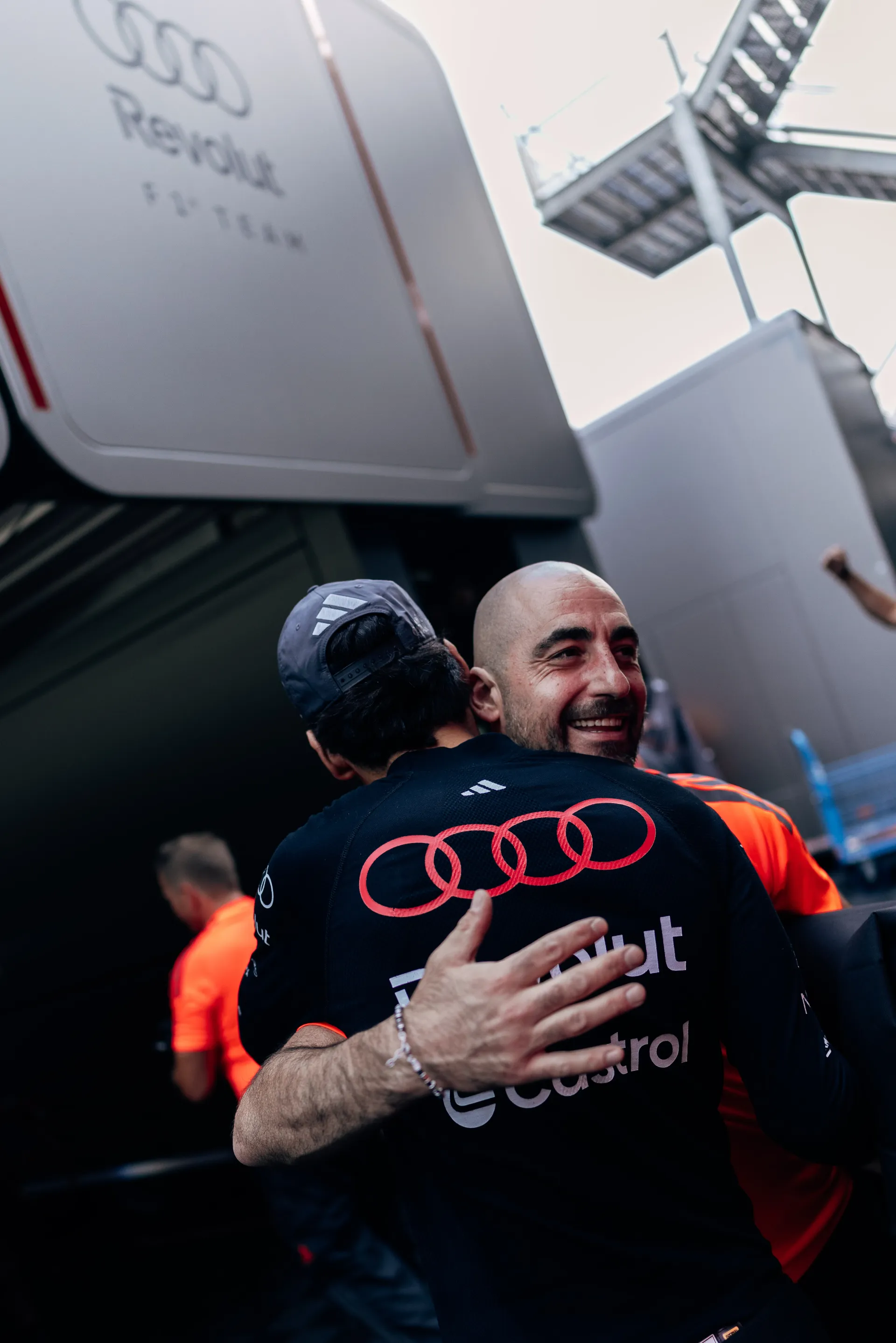 Audi Revolut F1® Team member embracing Gabriel Bortoleto near the team structure with paddock activity in the background