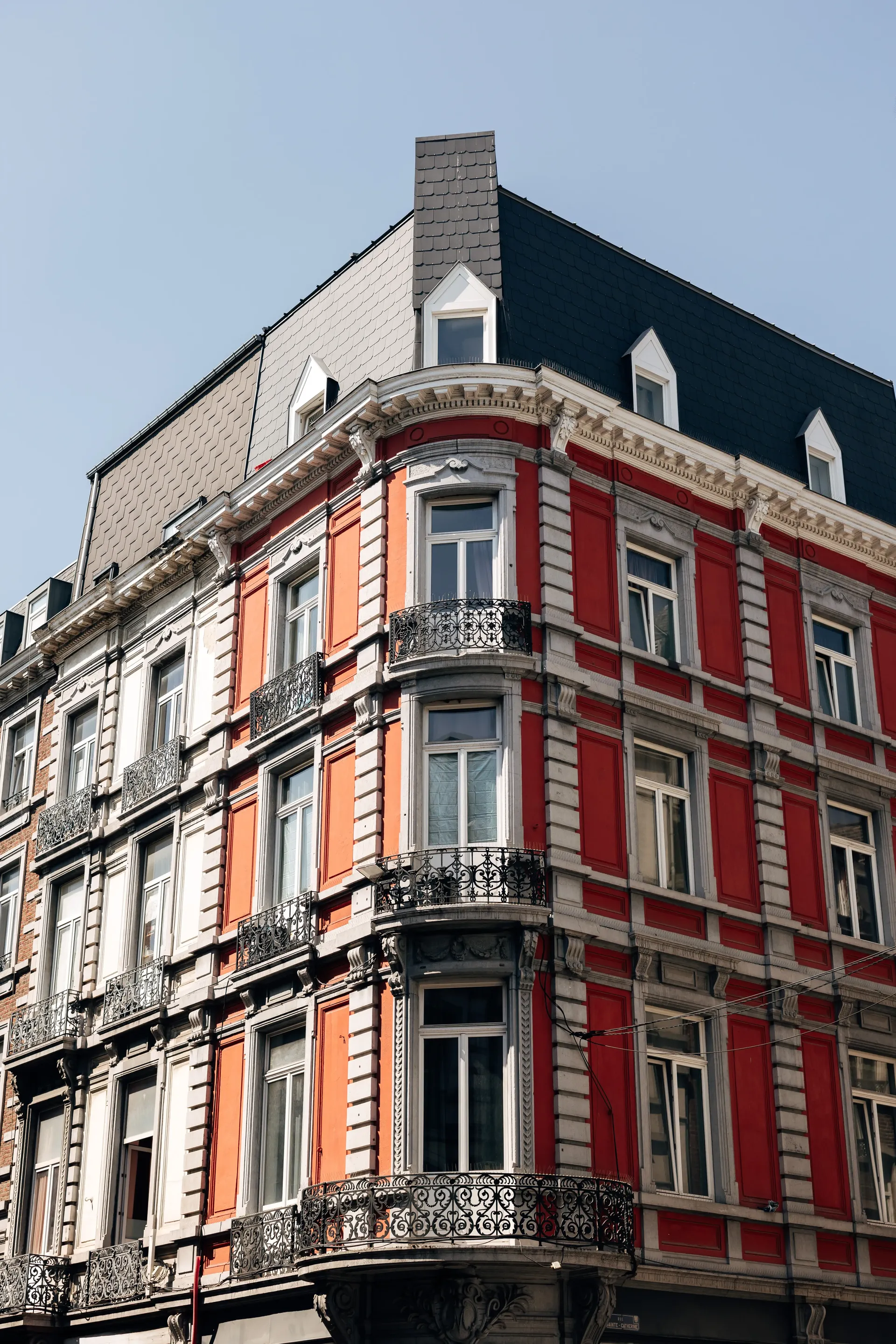 Historic red-and-white corner building with ornate balconies and classic Belgian architecture under blue skies.