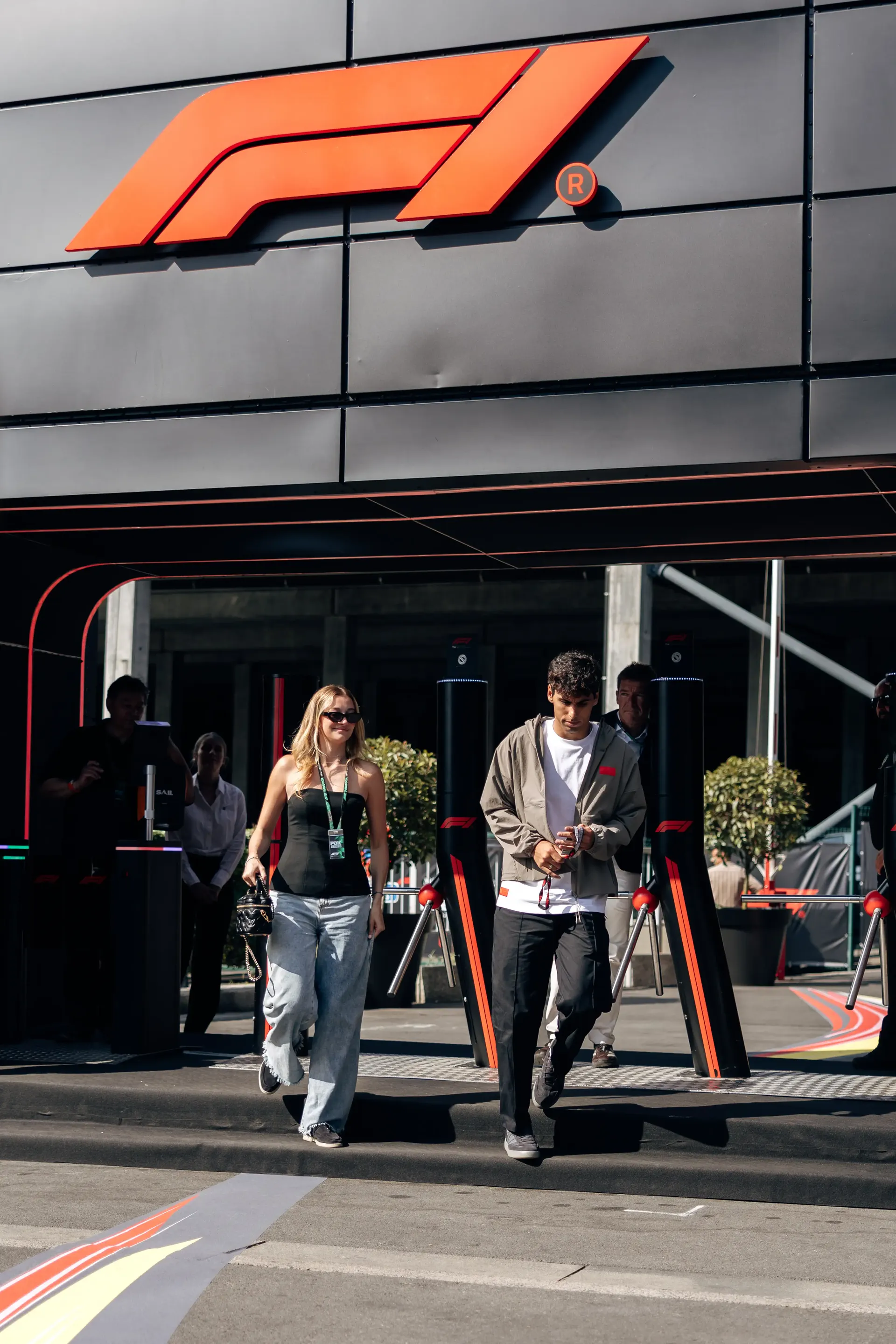 Gabriel Bortoleto, Audi Revolut F1® Team driver, arrives at the paddock with his girlfriend, smiling in a casual elevated fanwear outfit.
