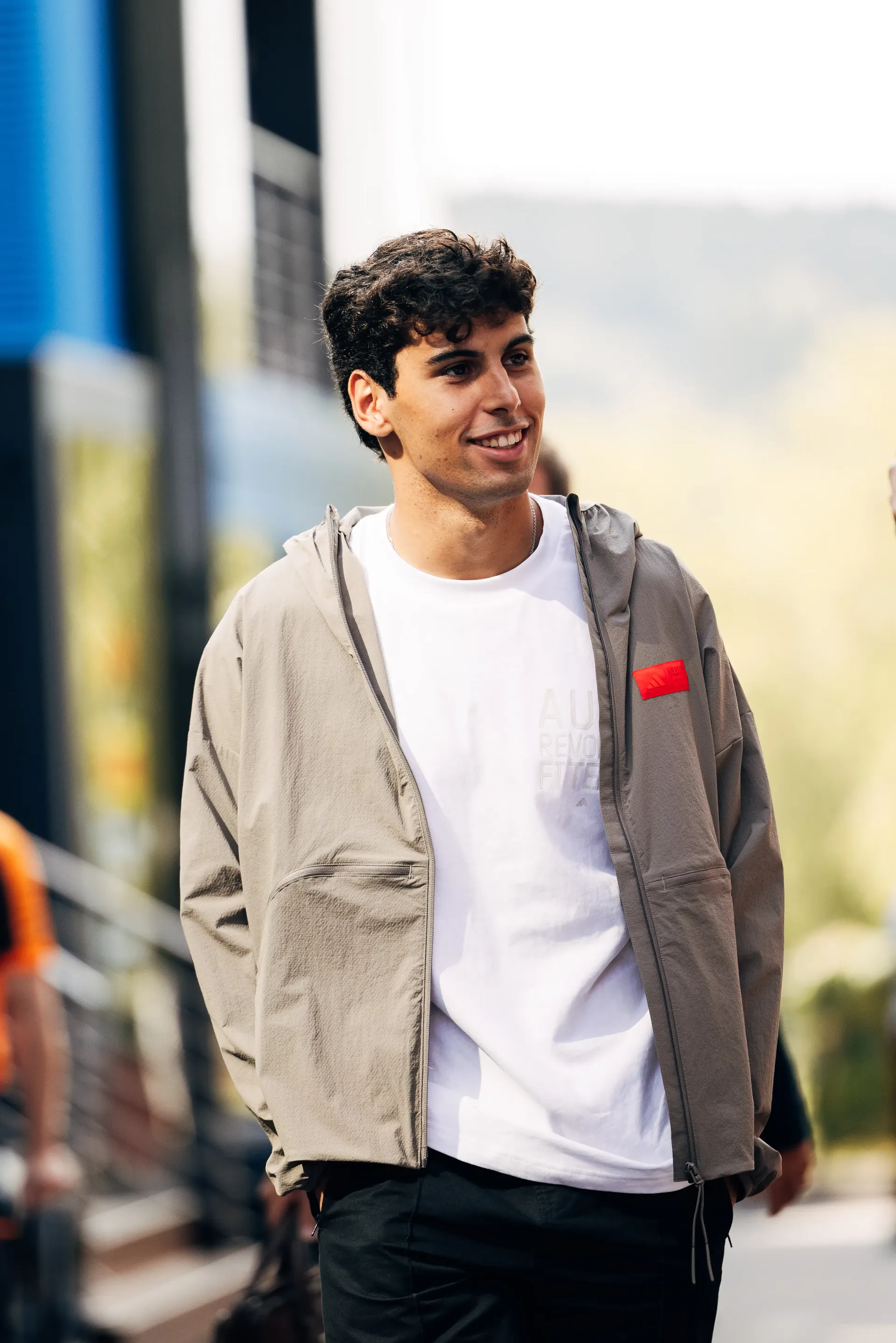 Gabriel Bortoleto, Audi Revolut F1® Team driver, arrives at the paddock, smiling in a casual elevated fanwear outfit.