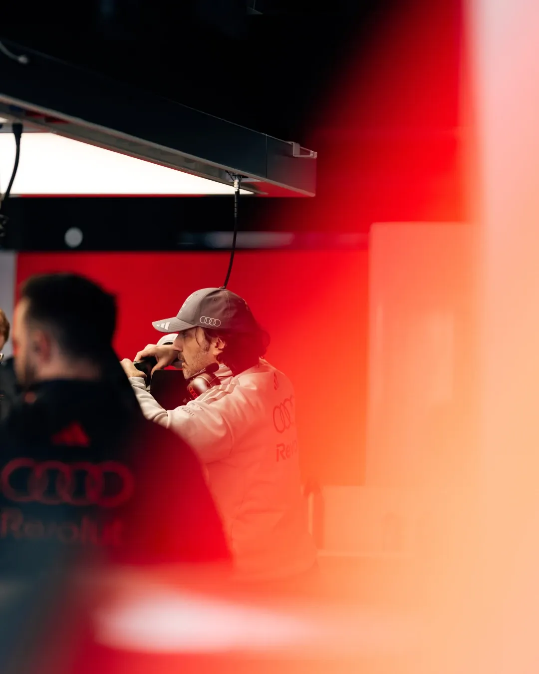 Team member in Audi Revolut F1® Team apparel observing garage operations, partially obscured by red light flare.