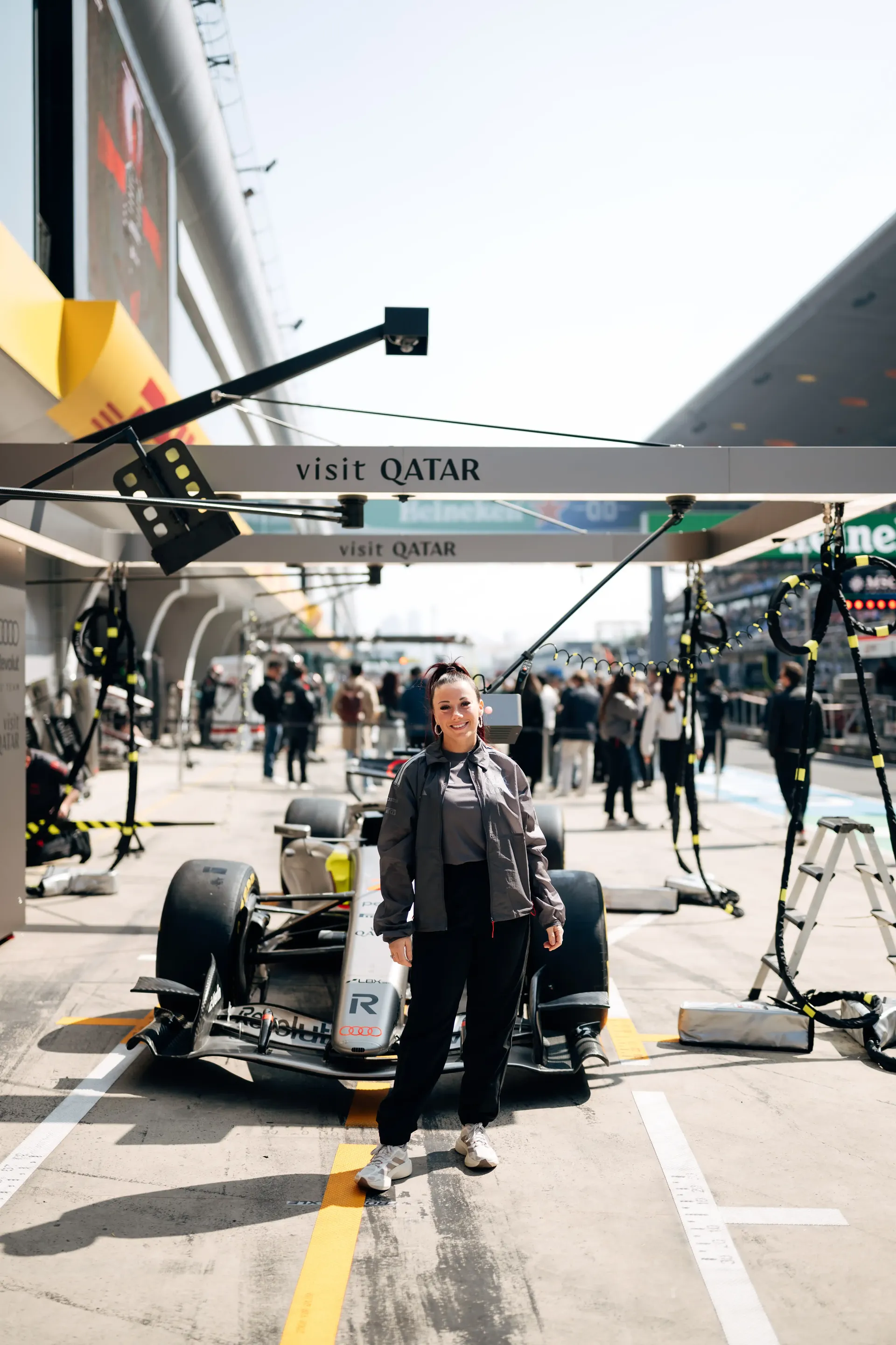 Carrie Schreiner standing in front of Audi Revolut F1® Team Academy Formula 1® car in the pit lane, posing confidently with the race car behind her.